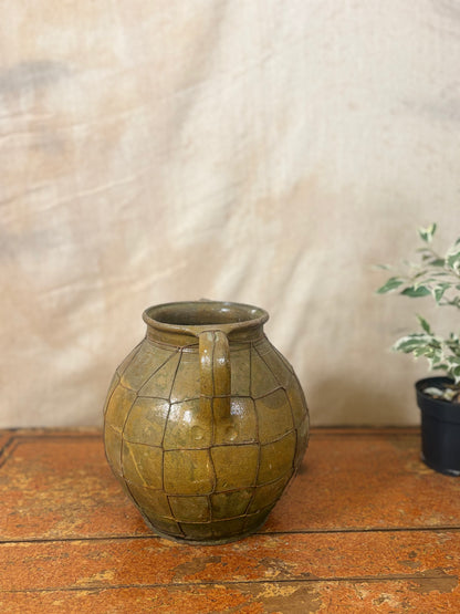 Vintage green ceramic jar with a textured surface on a wooden surface.