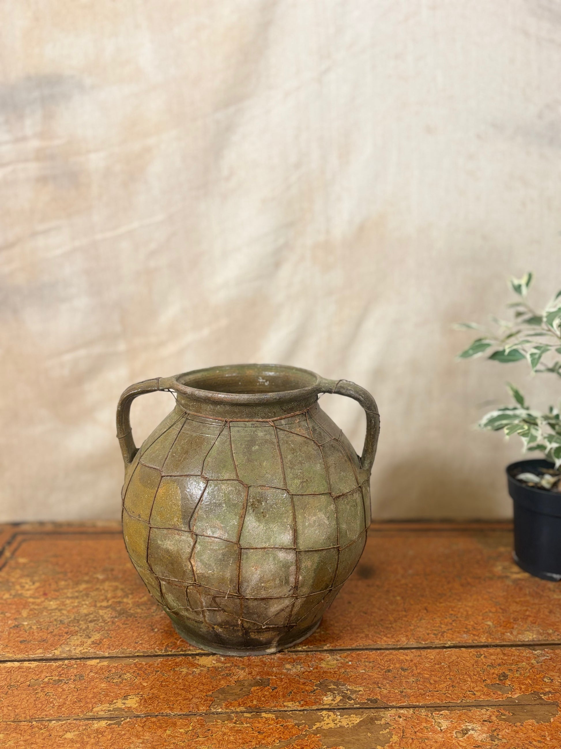 Vintage green ceramic vase with two handles on a wooden surface with a neutral background