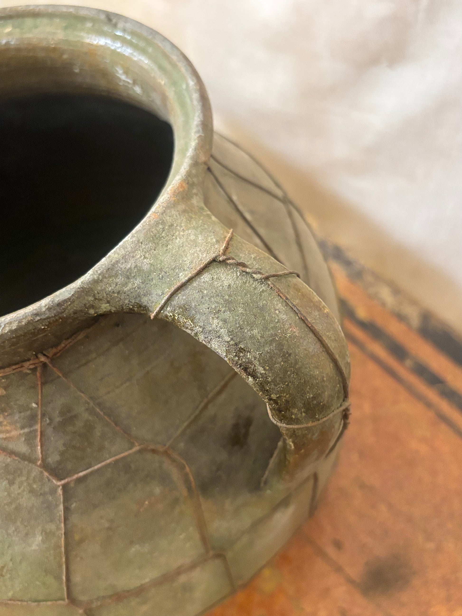 Close-up of a green ceramic vase with textured surface on a wooden floor.