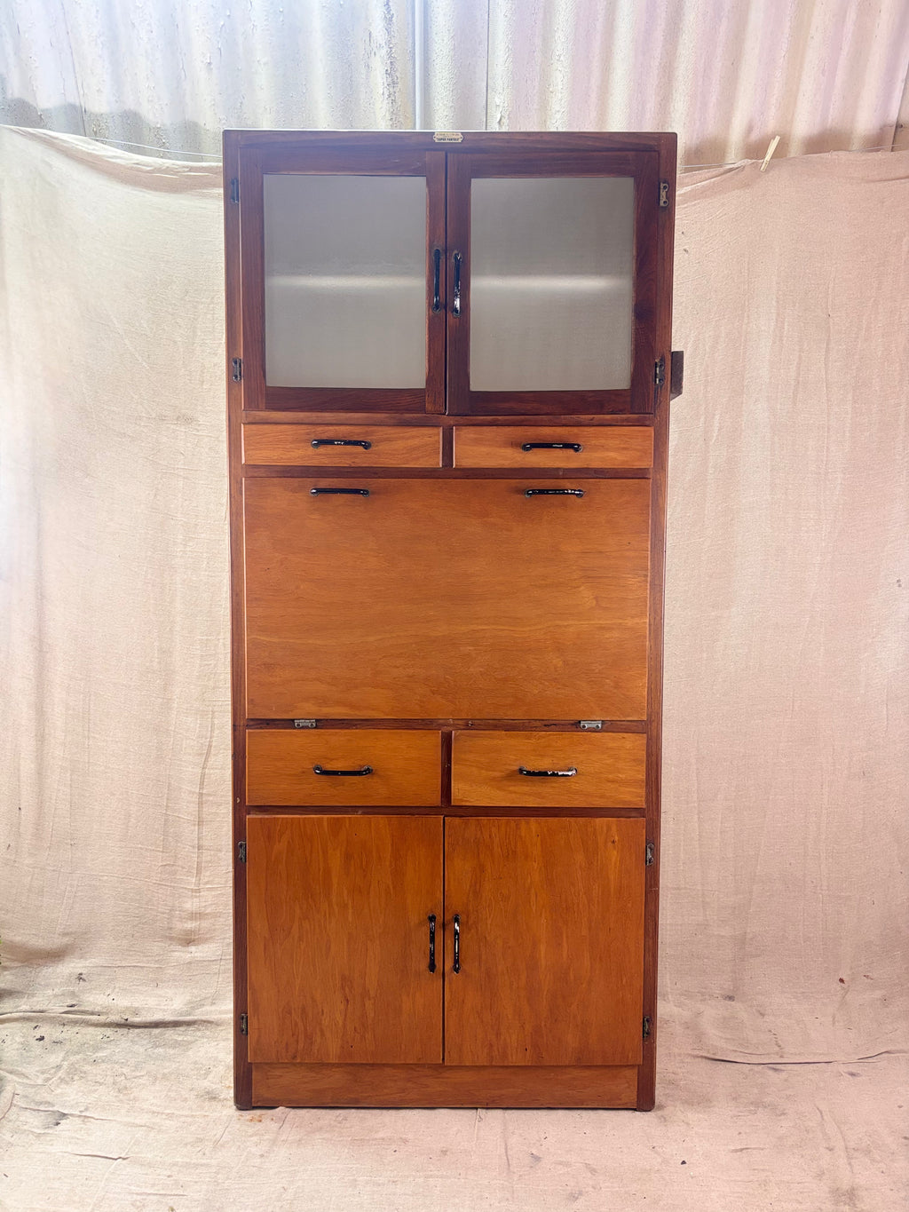 Wooden cabinet with glass doors and drawers against a plain background