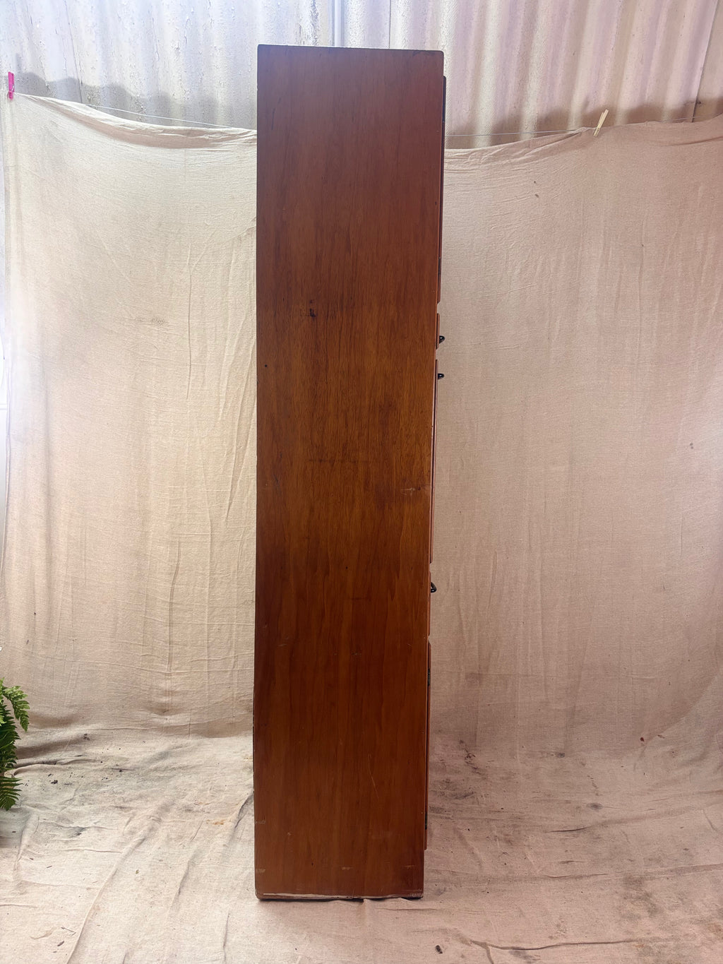 Tall wooden cabinet against a plain white curtain background