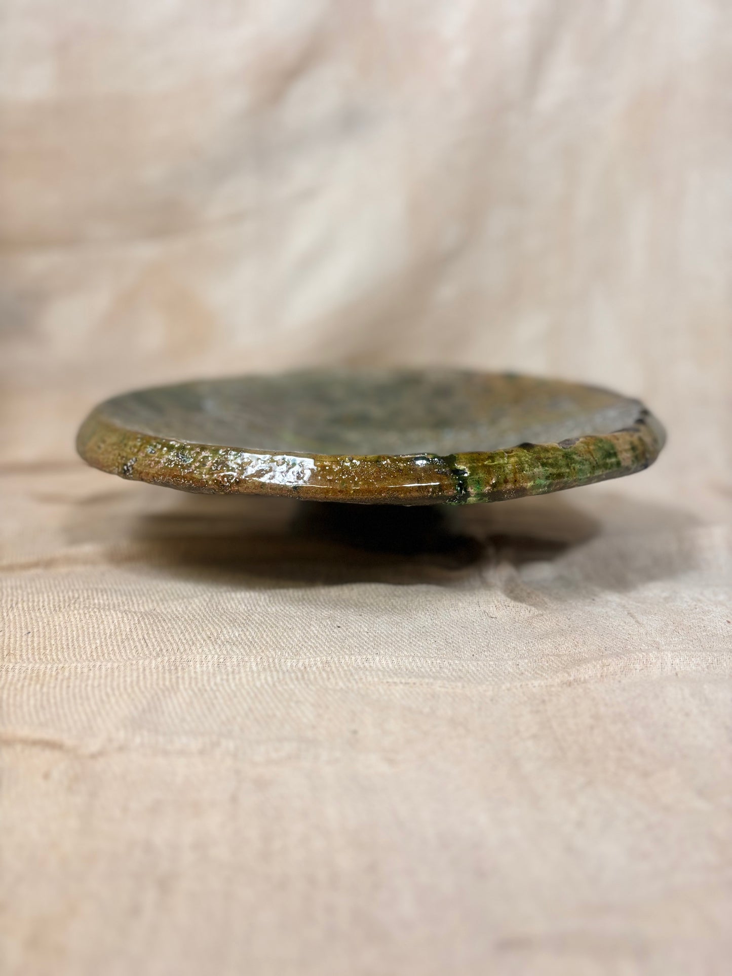 Round ceramic plate with green glaze on a beige fabric background