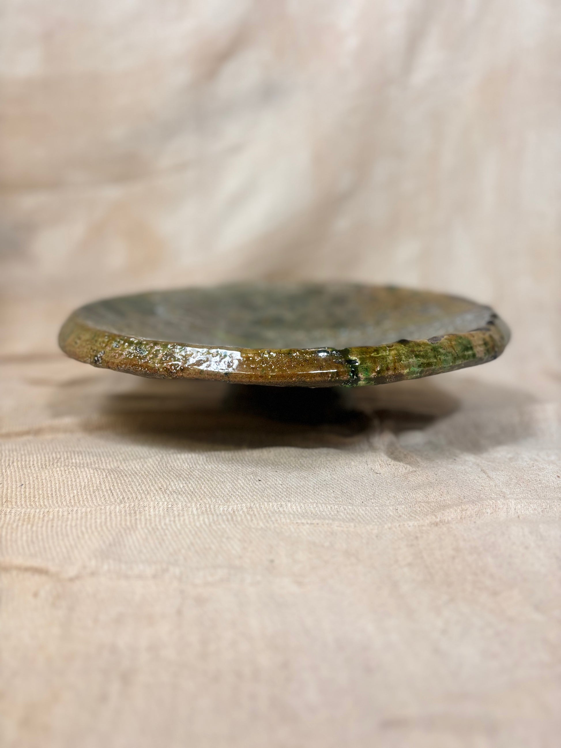 Round ceramic plate with green glaze on a beige fabric background
