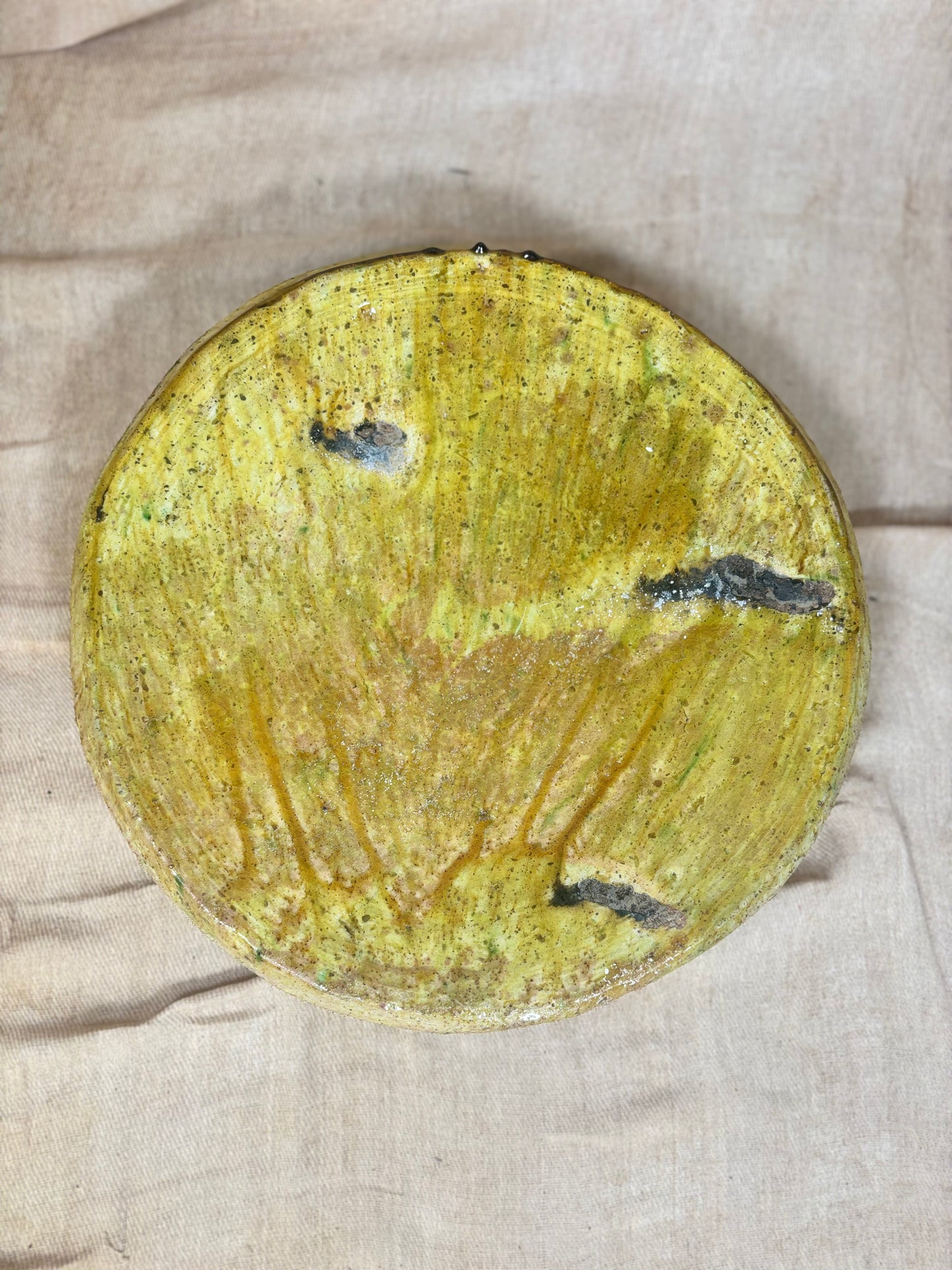 Round yellowish plate with black spots on a beige fabric background