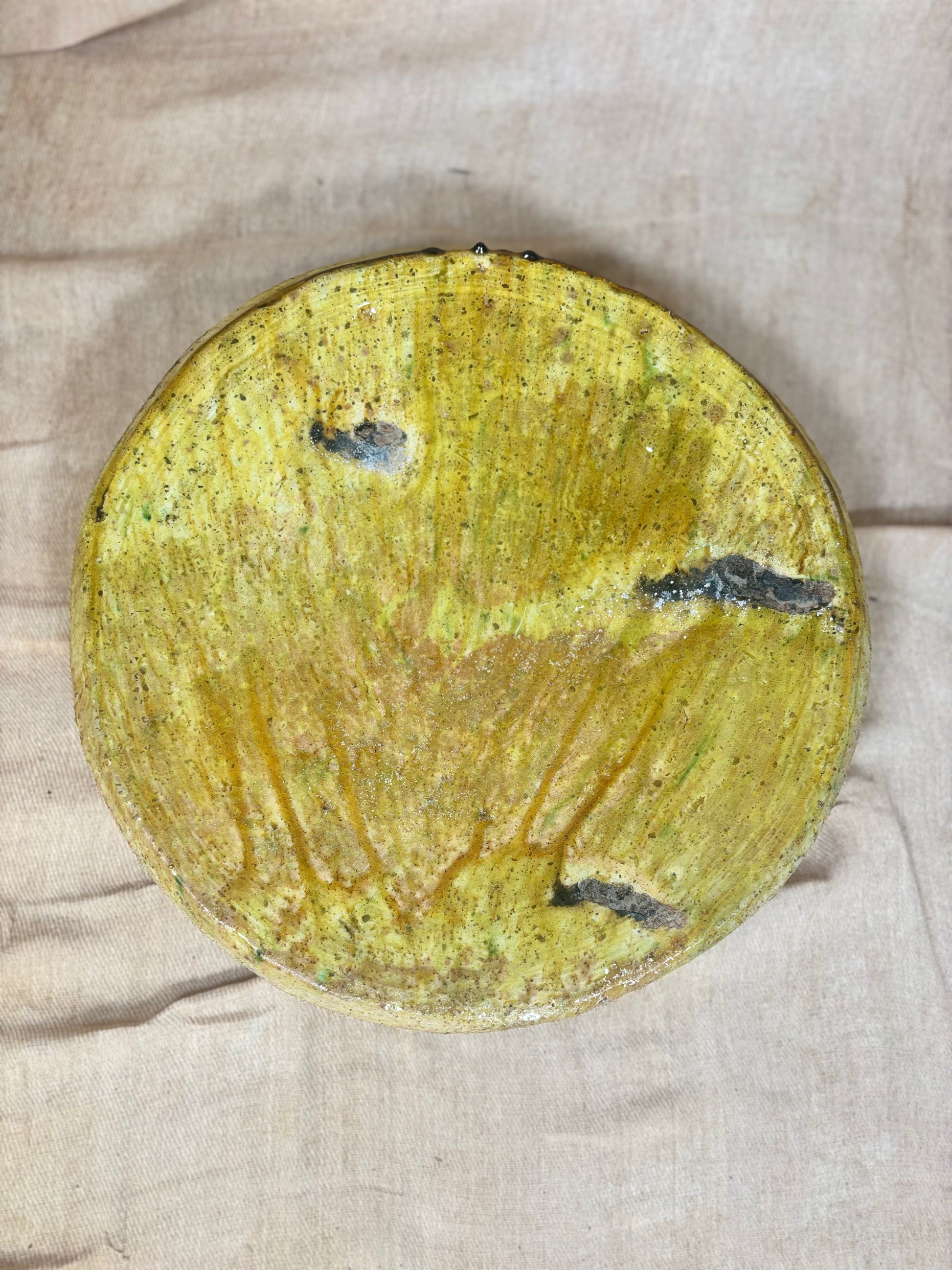 Round yellowish plate with black spots on a beige fabric background