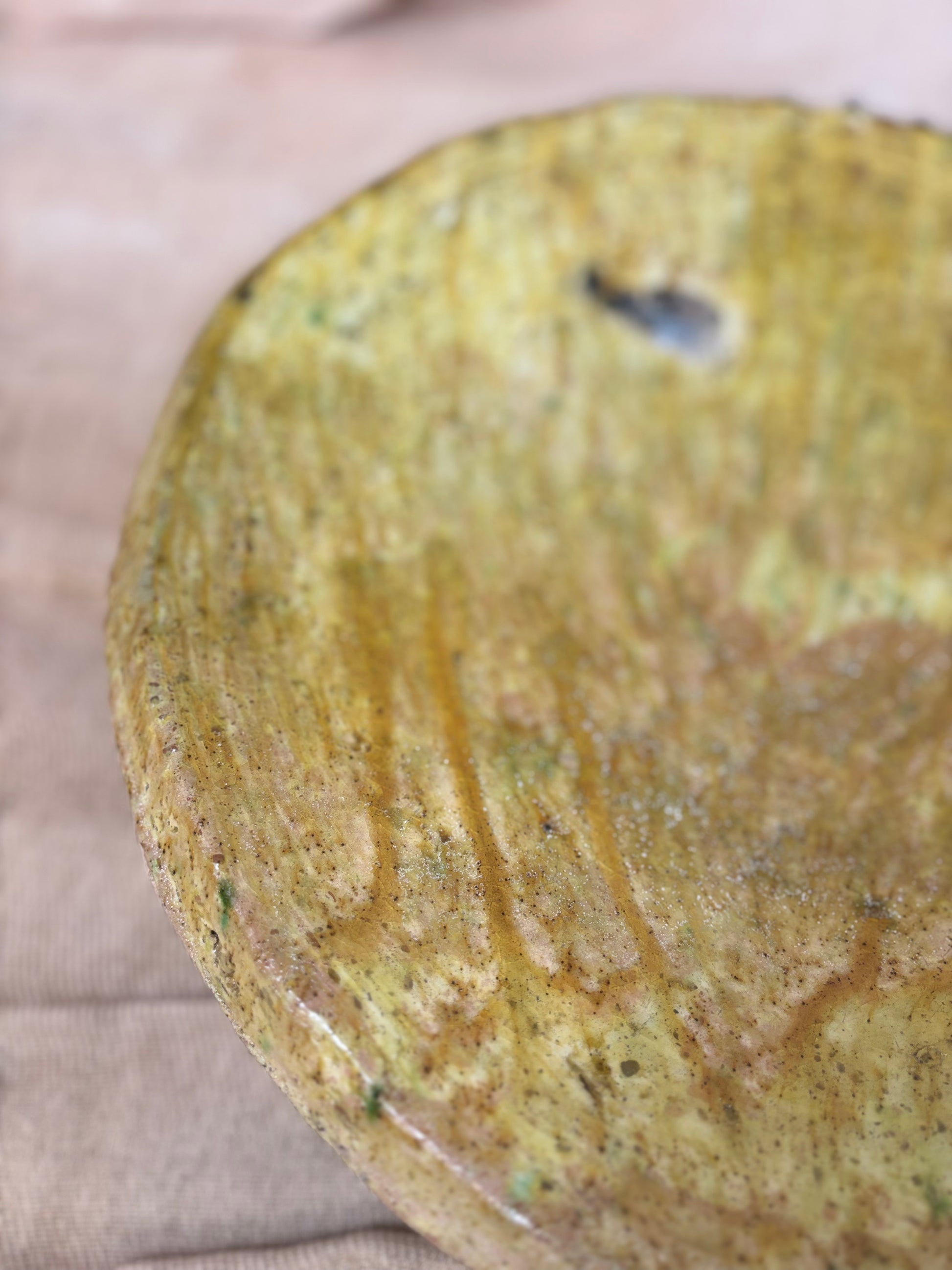 Close-up of a textured yellowish-brown ceramic plate on a beige surface
