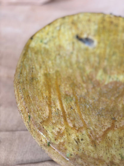 Close-up of a textured yellowish-brown ceramic plate on a beige surface