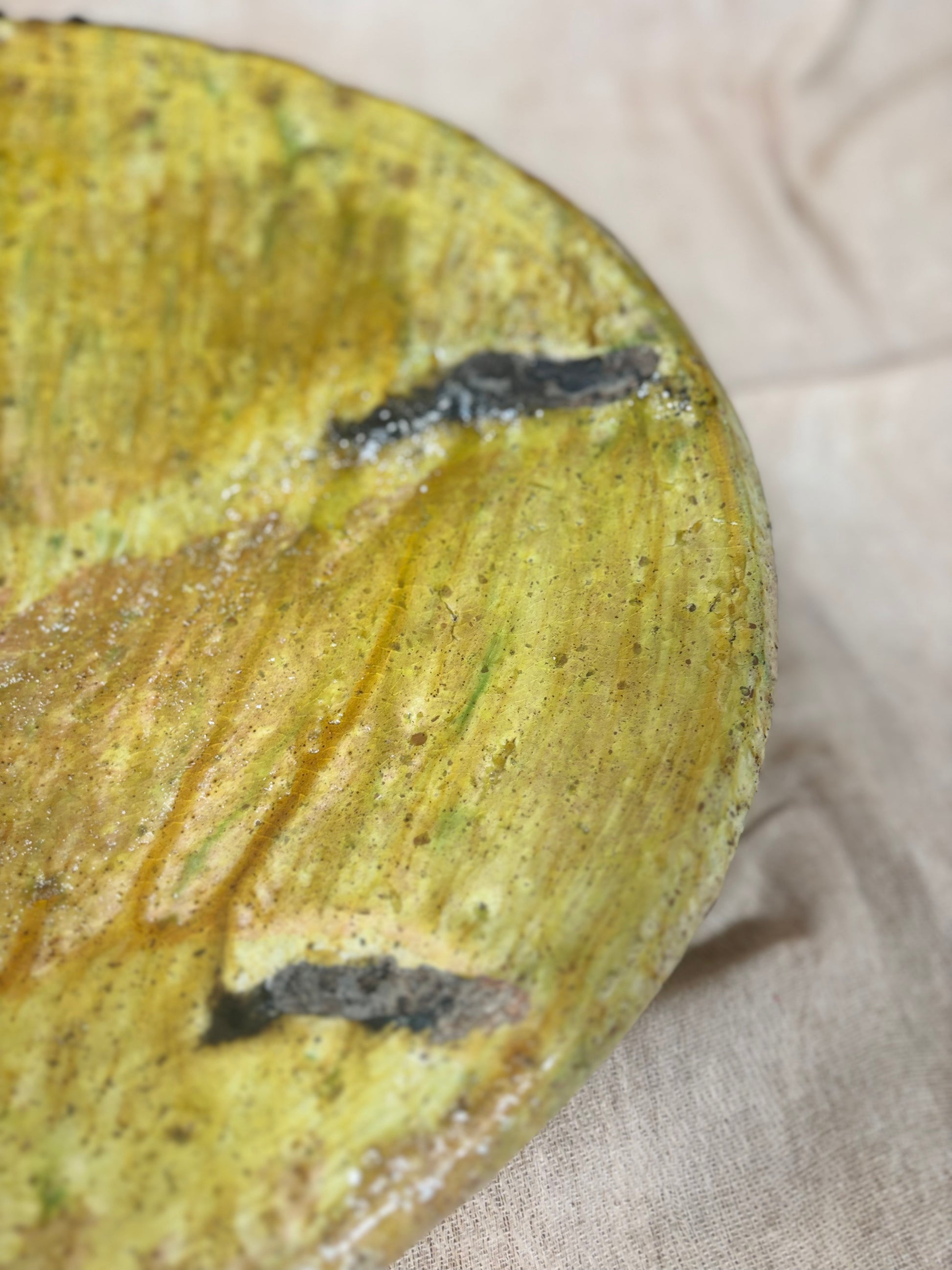 Close-up of a textured yellow and green ceramic plate on a beige fabric background
