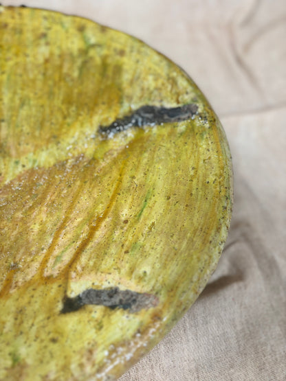 Close-up of a textured yellow and green ceramic plate on a beige fabric background