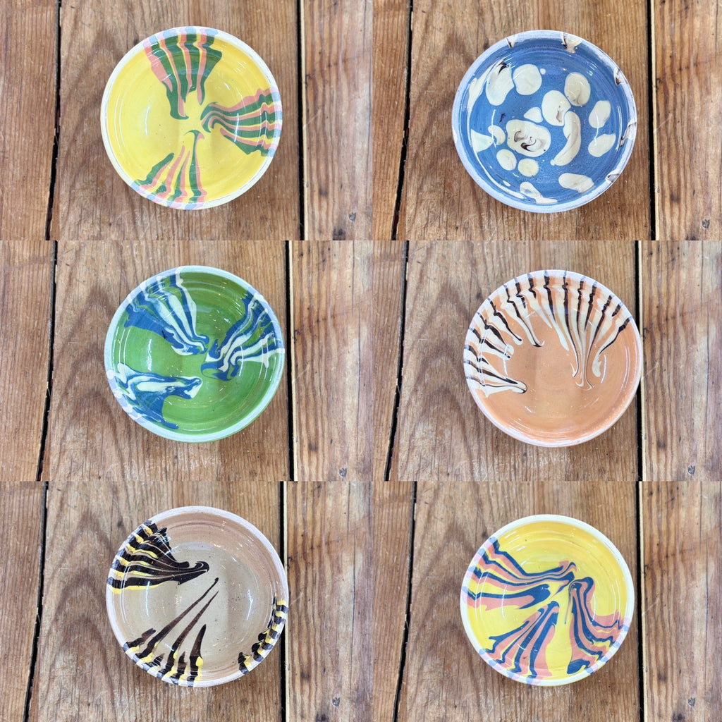 Set of six small ceramic bowls with various artistic designs on a wooden surface