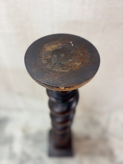 A tall, dark wooden pedestal or plant stand featuring a prominent barley twist central column and a square base.