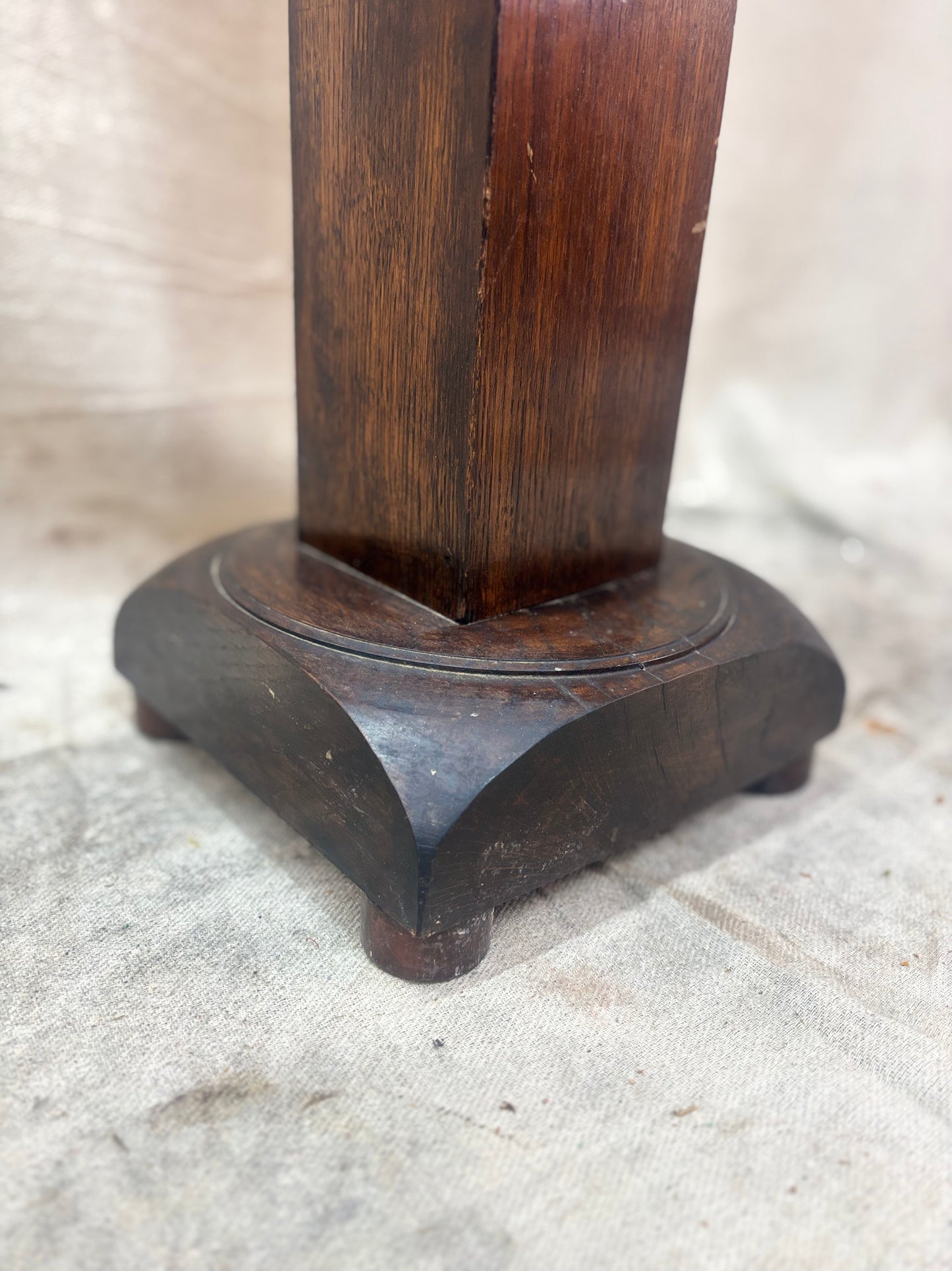 A tall, dark wooden pedestal or plant stand featuring a prominent barley twist central column and a square base.