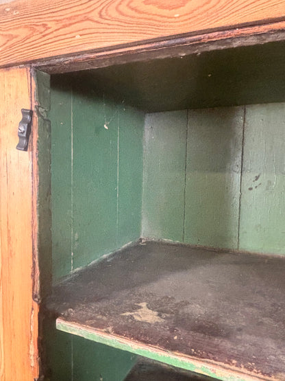 Close-up of a rustic wooden cabinet or shelf unit with a green painted interior, a dark shelf surface, and a visible metal latch on the left side.