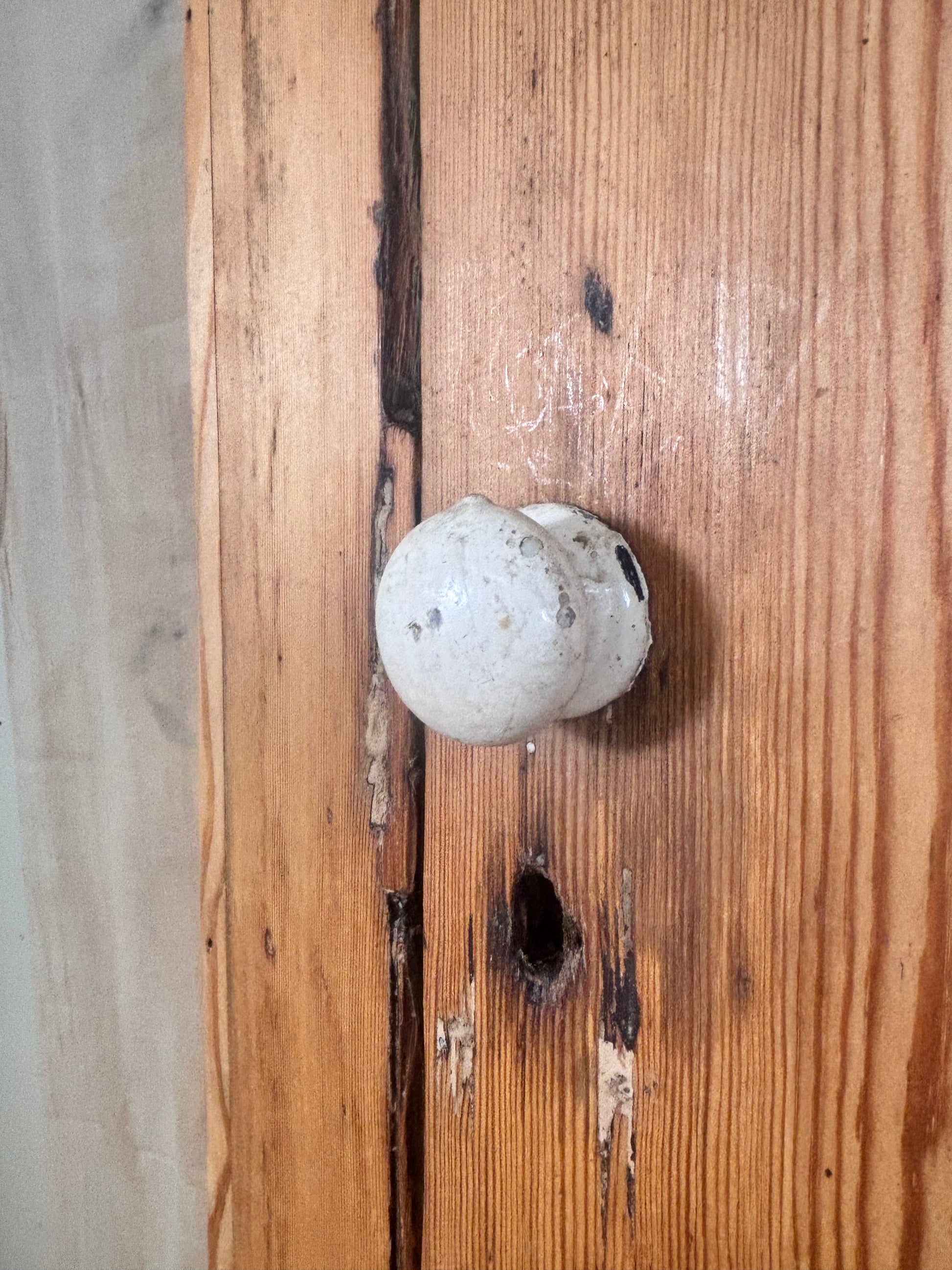 A round, vintage-style off-white ceramic doorknob with dark speckles, mounted on a rustic wooden door.