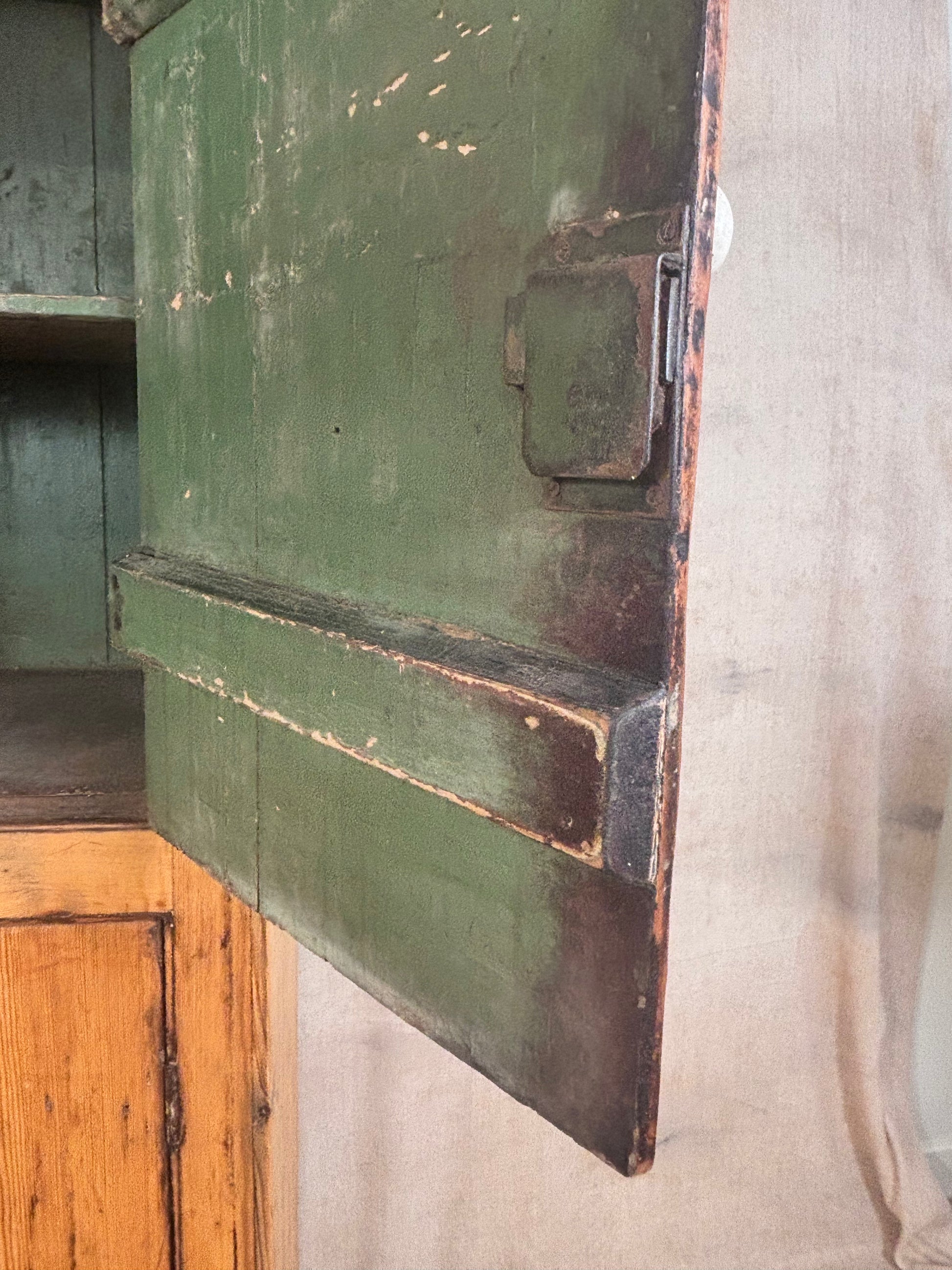 Close-up of a distressed green wooden cabinet door with a metal latch, showing peeling paint and weathered edges, set against a neutral fabric background.