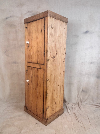 A rustic pine wood storage cabinet with two doors and small white knobs, standing against a draped fabric backdrop.