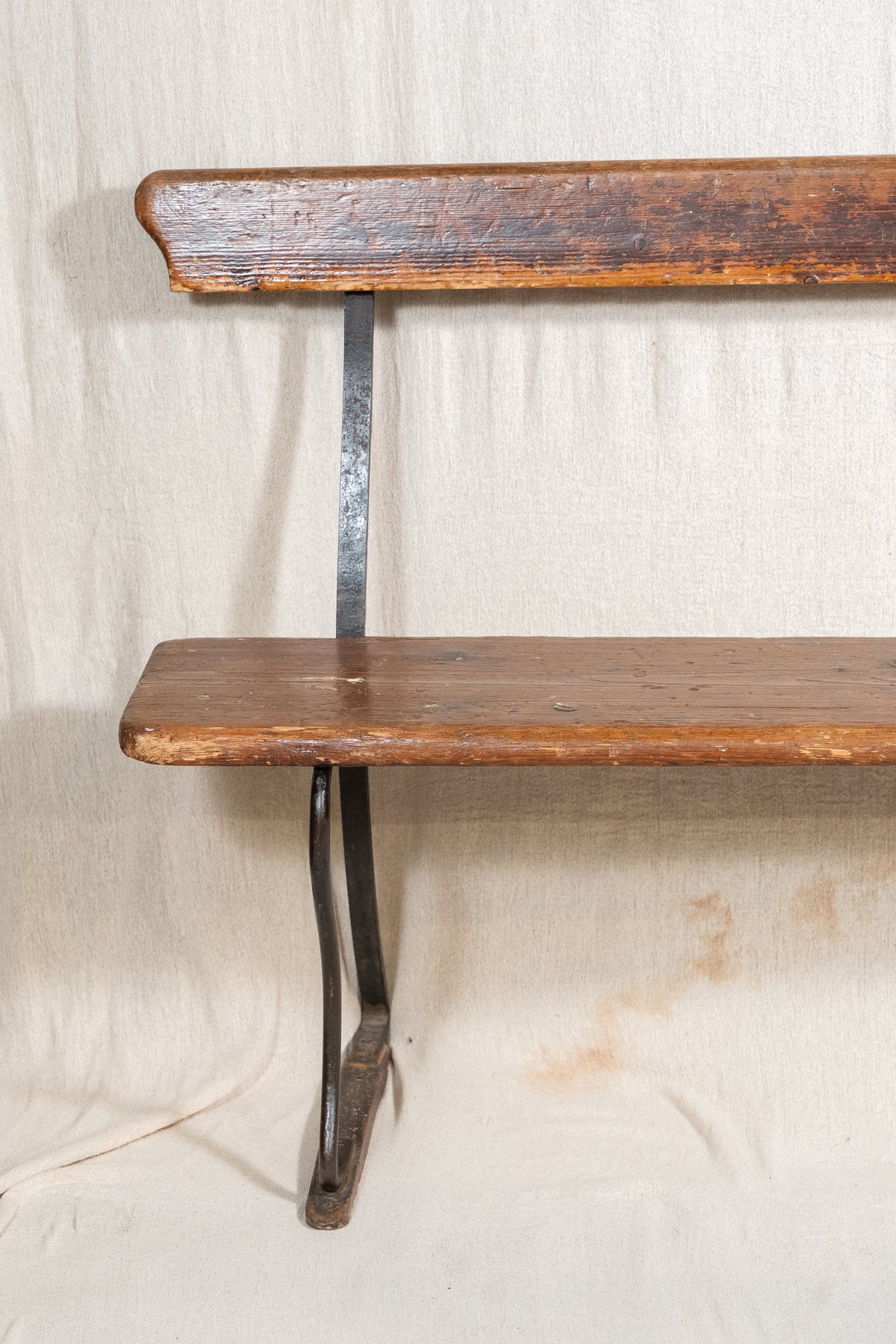 A rustic wooden wall shelf with a weathered brown finish and a dark metal bracket support, set against a draped beige fabric backdrop.