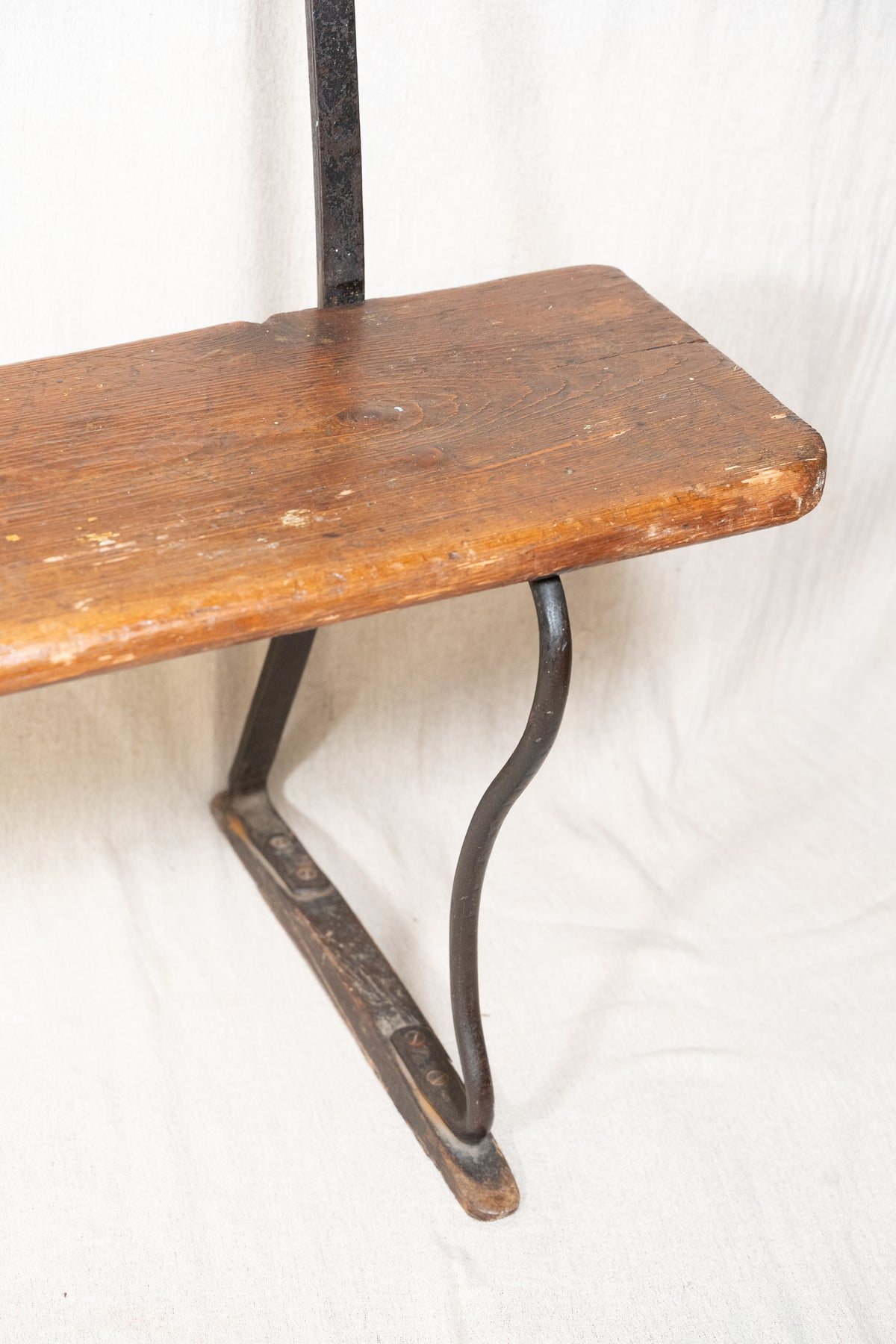 A rustic wooden bench with a weathered brown wood seat and a dark metal support frame, photographed against a white fabric backdrop.