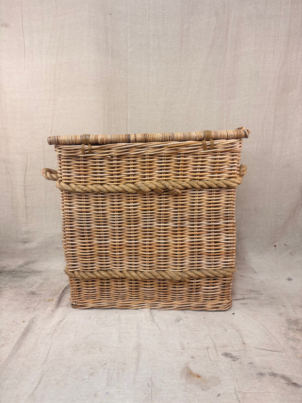 Square wicker storage basket with lid and rope banding, photographed against a neutral backdrop.