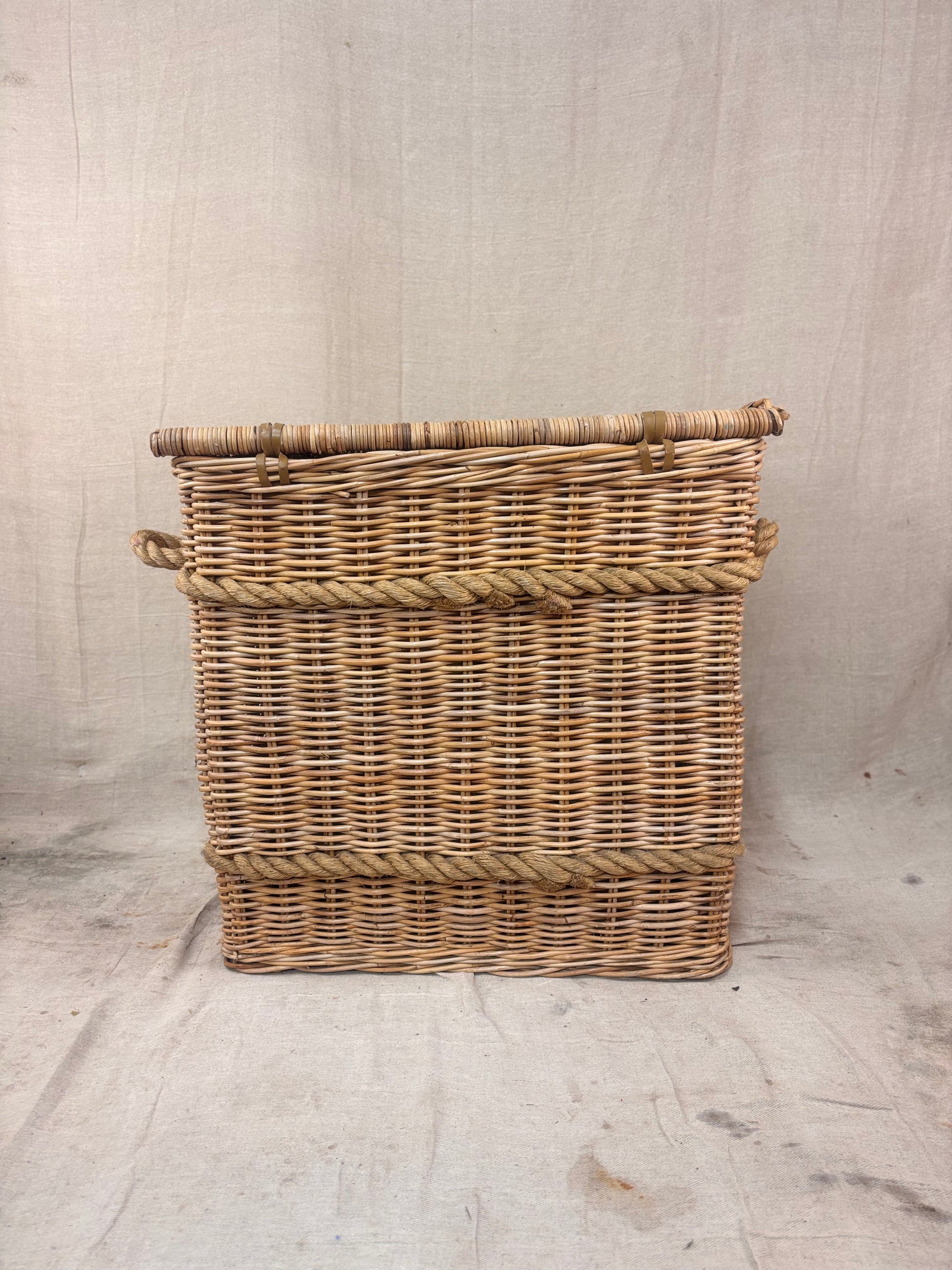Square wicker storage basket with lid and rope banding, photographed against a neutral backdrop.