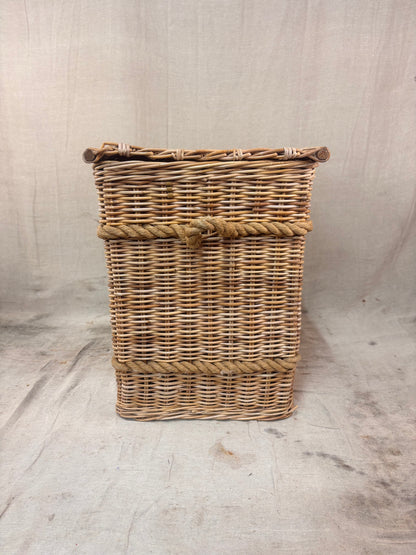 Square wicker storage basket with lid and rope banding, photographed against a neutral backdrop.