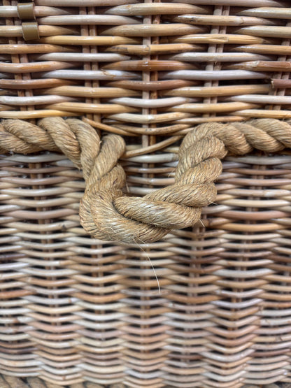 Large wicker storage basket with lid and rope banding, photographed against a neutral backdrop.