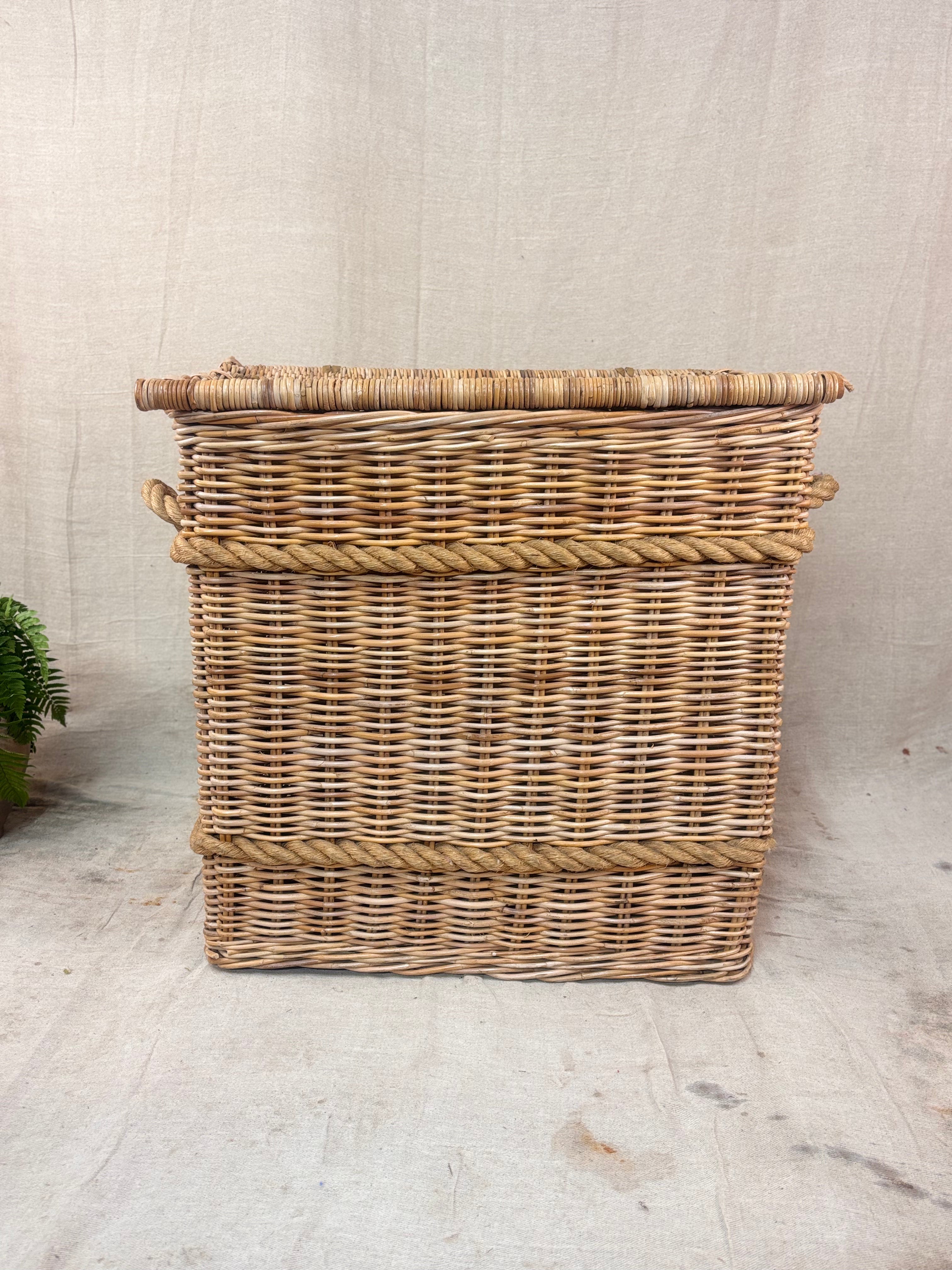 Large wicker storage basket with lid and rope banding, photographed against a neutral backdrop.