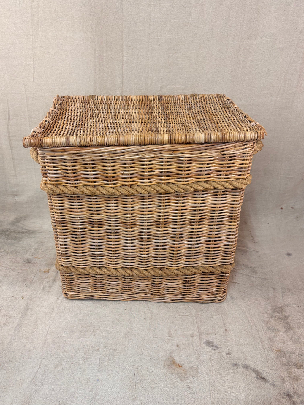 Large wicker storage basket with lid and rope banding, photographed against a neutral backdrop.