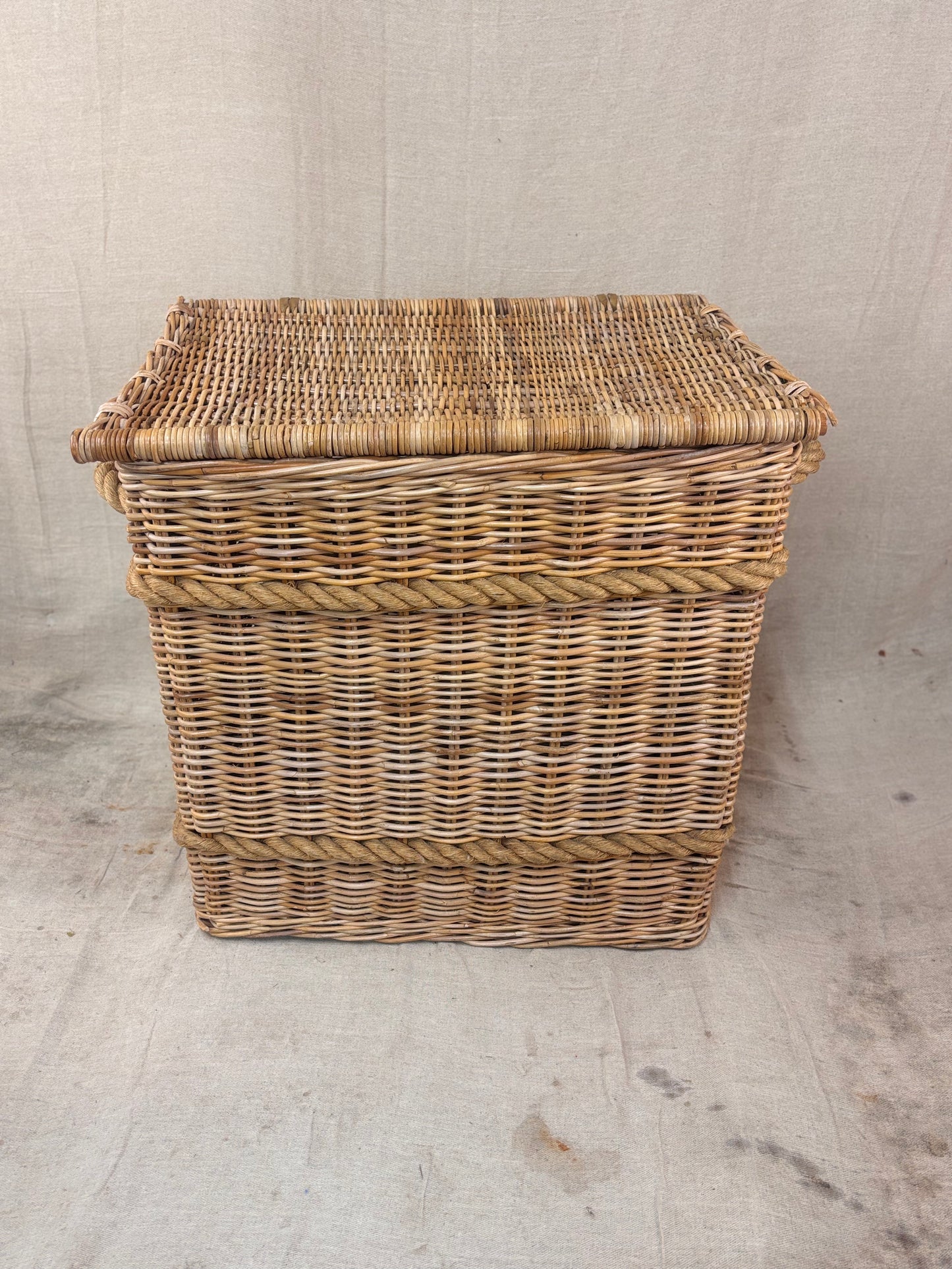 Large wicker storage basket with lid and rope banding, photographed against a neutral backdrop.