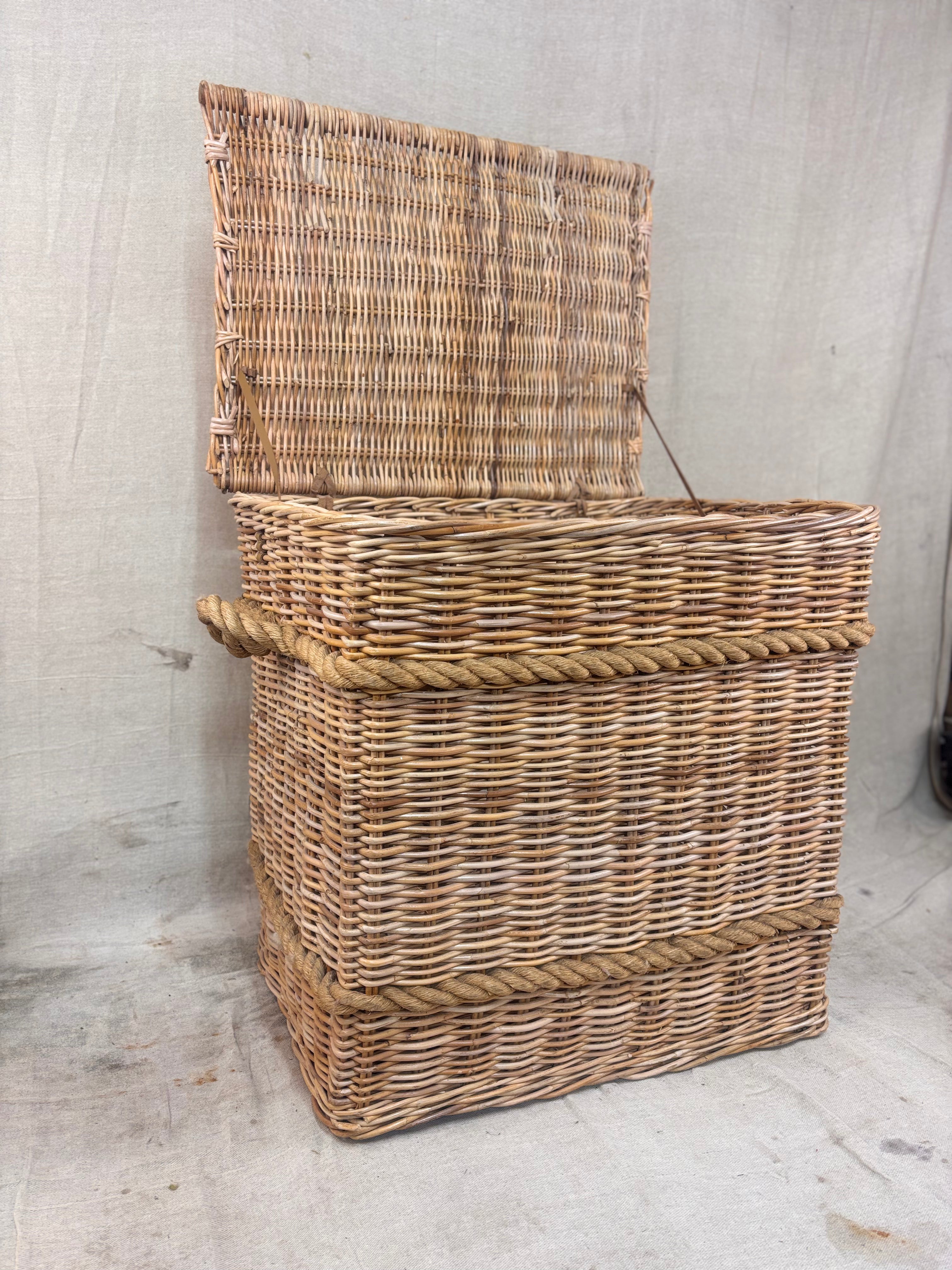 Square wicker storage basket with lid and rope banding, photographed against a neutral backdrop.