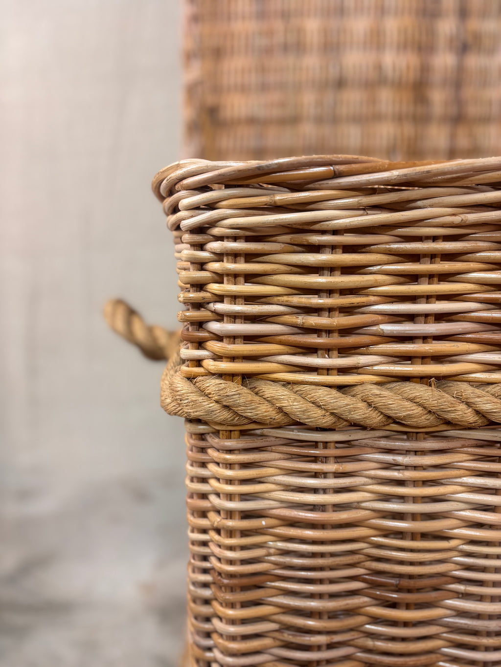Large wicker storage basket with lid and rope banding, photographed against a neutral backdrop.