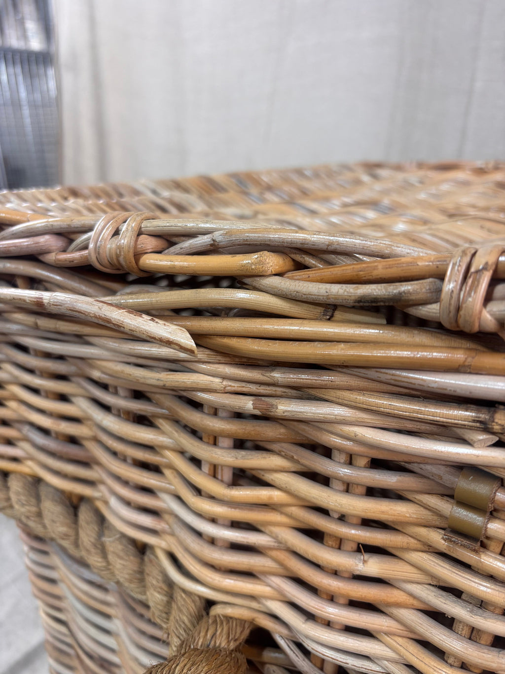 Large wicker storage basket with lid and rope banding, photographed against a neutral backdrop.