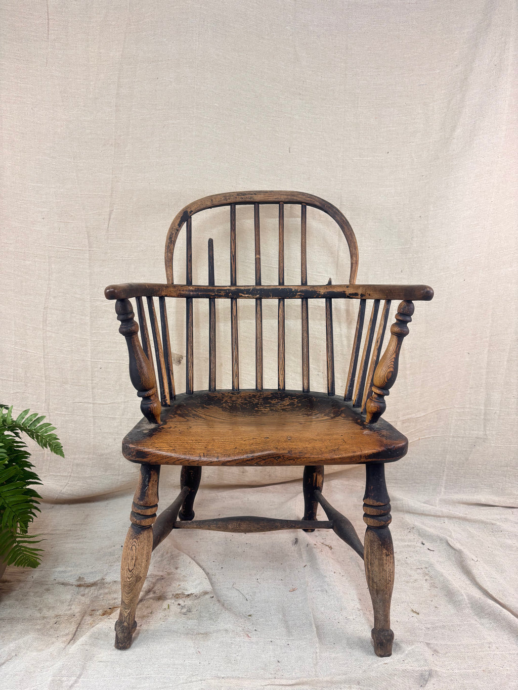 Windsor chair with hoop back, saddled seat, and splayed turned legs shown against a cream fabric background.