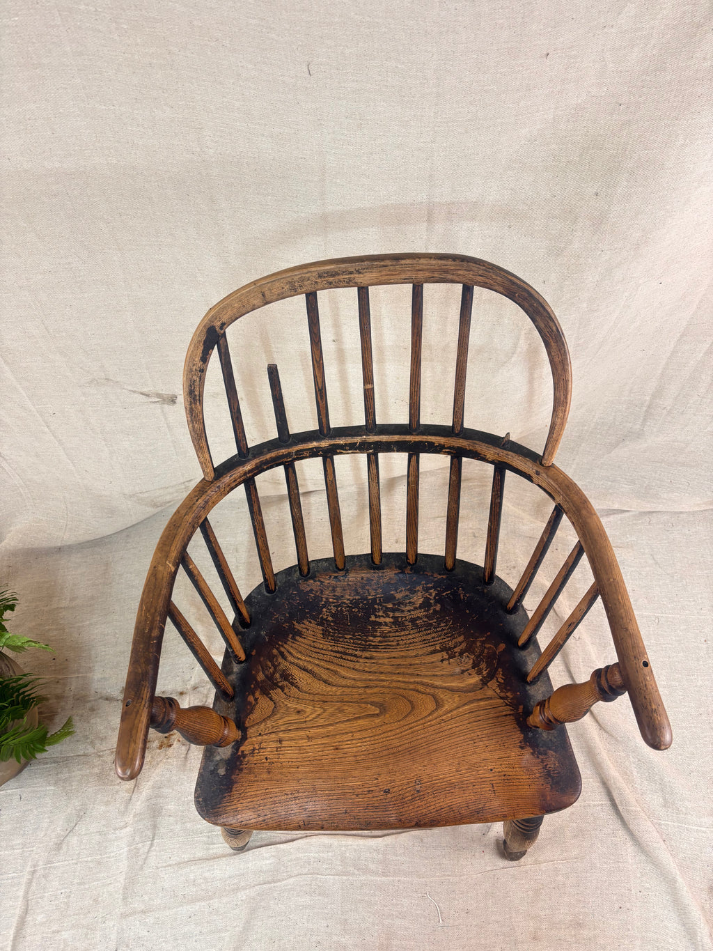 Windsor chair with hoop back, saddled seat, and splayed turned legs shown against a cream fabric background.
