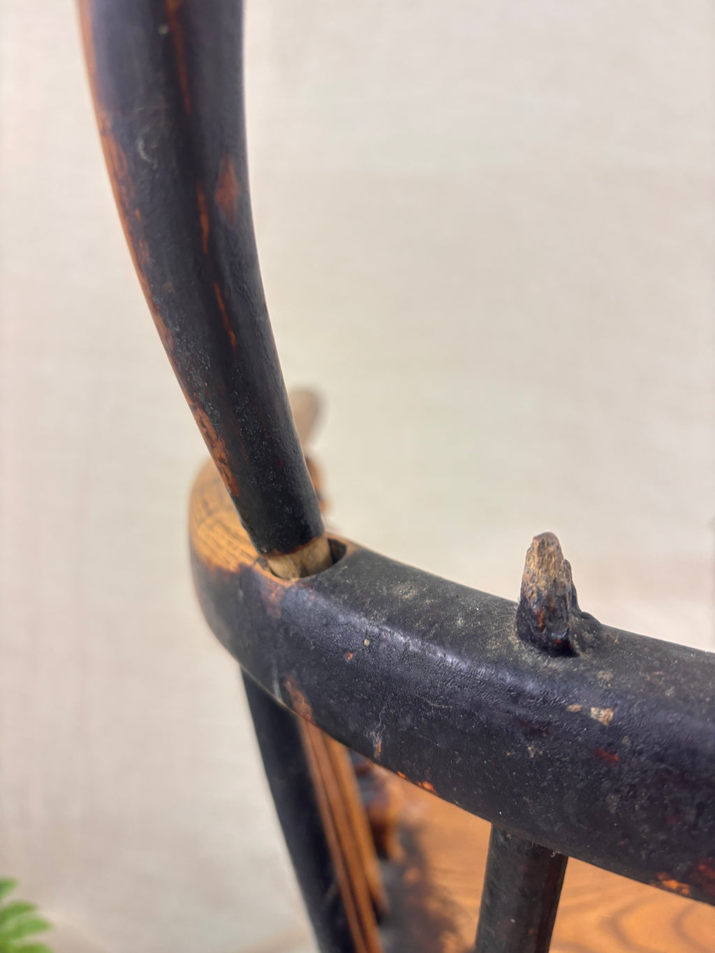 Detail of damage to back of Windsor chair with hoop back, shown against a cream fabric background.
