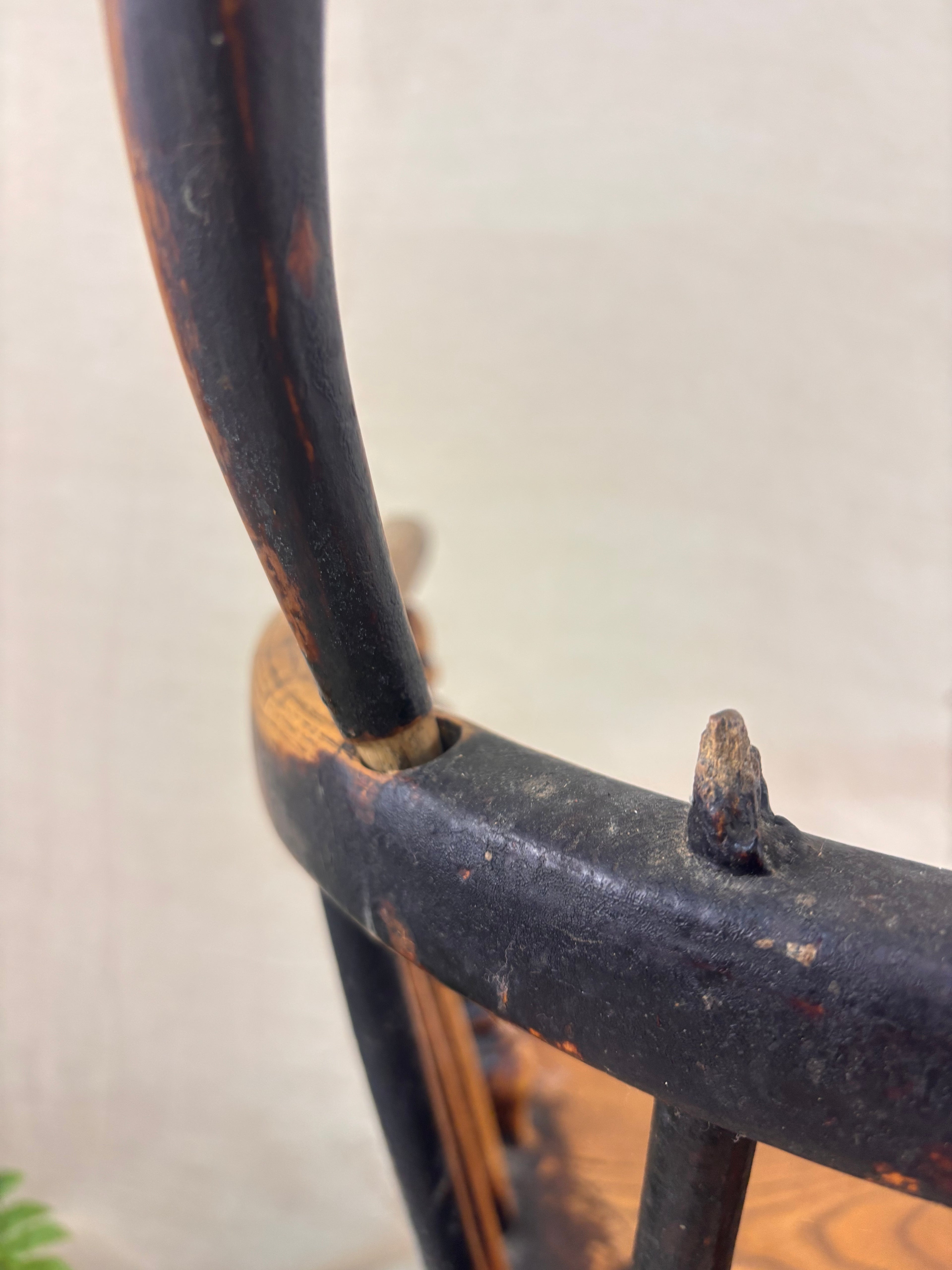 Detail of damage to back of Windsor chair with hoop back, shown against a cream fabric background.
