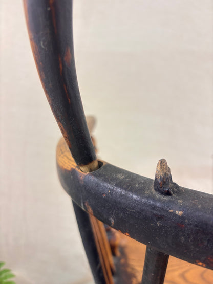 Detail of damage to back of Windsor chair with hoop back, shown against a cream fabric background.
