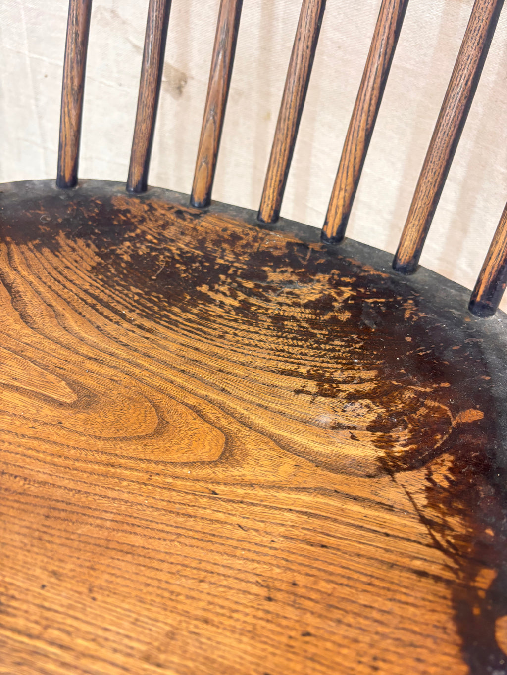 Windsor chair with hoop back, saddled seat, shown against a cream fabric background.
