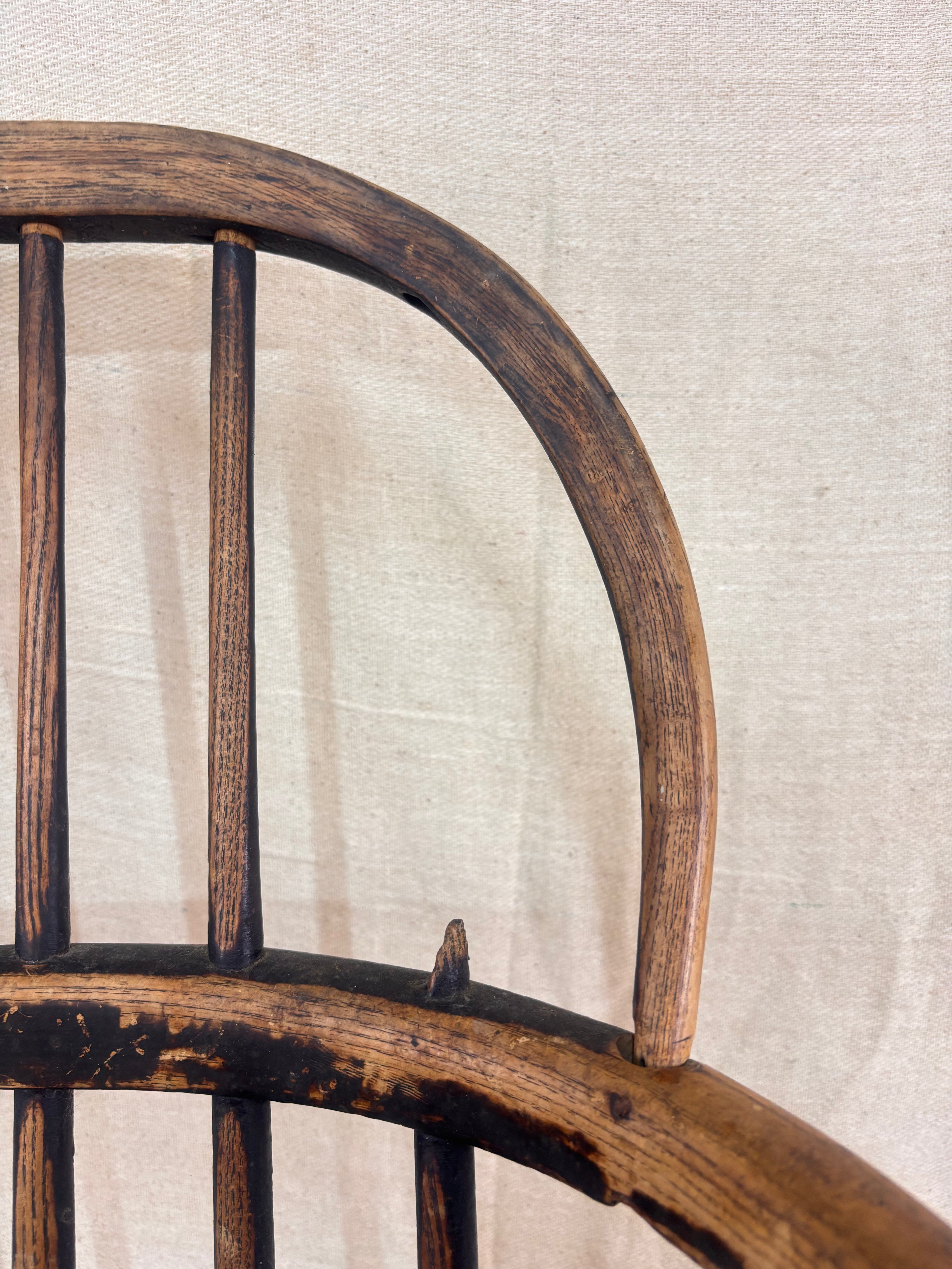 Detail of damage to Windsor chair with hoop back, shown against a cream fabric background.
