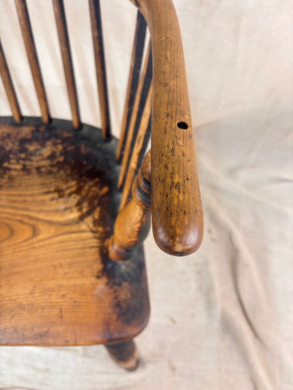 Windsor chair with hoop back, saddled seat, and splayed turned legs shown against a cream fabric background.