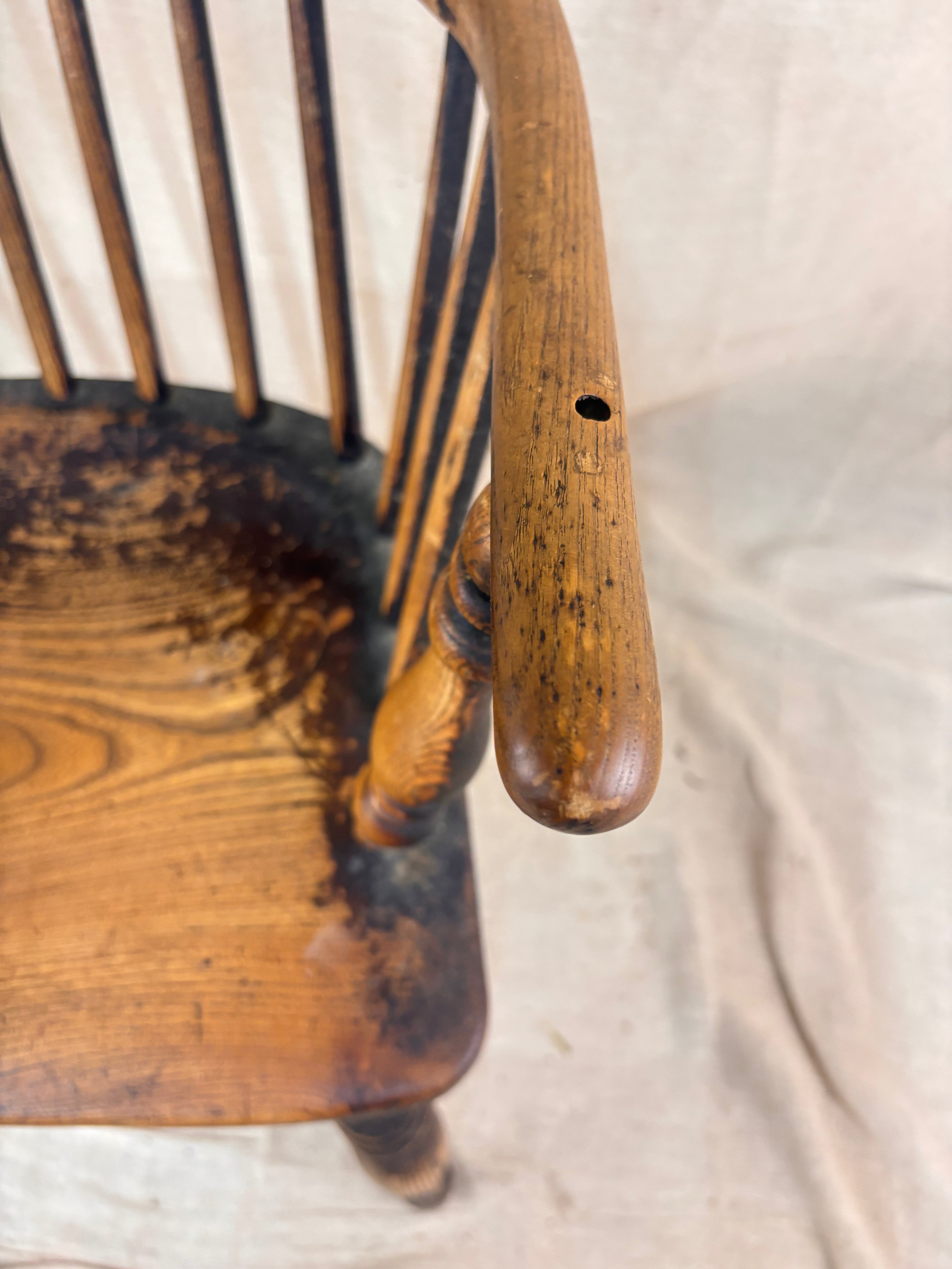 Windsor chair with hoop back, saddled seat, and splayed turned legs shown against a cream fabric background.