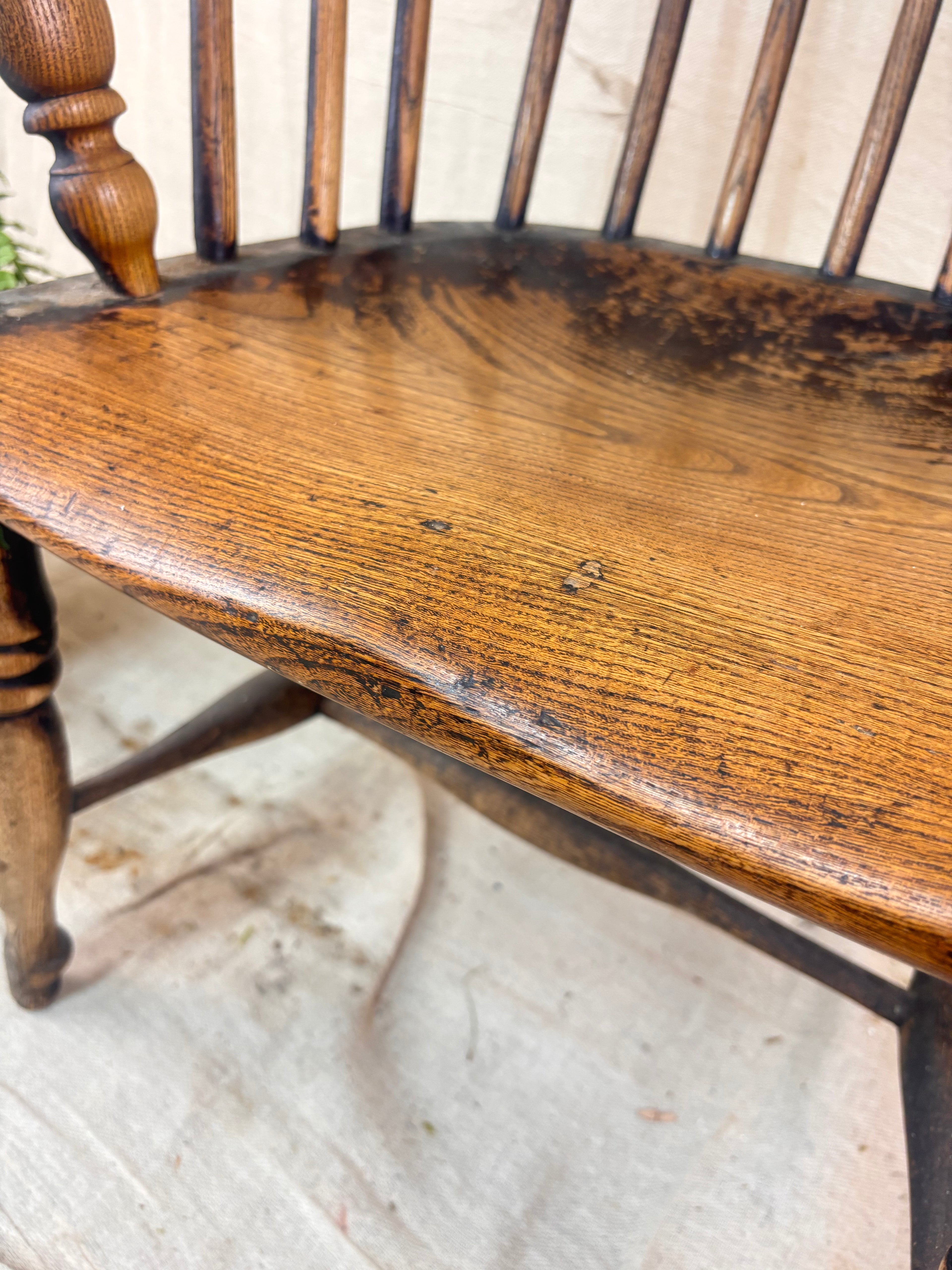 Windsor chair with hoop back, saddled seat, and splayed turned legs shown against a cream fabric background.
