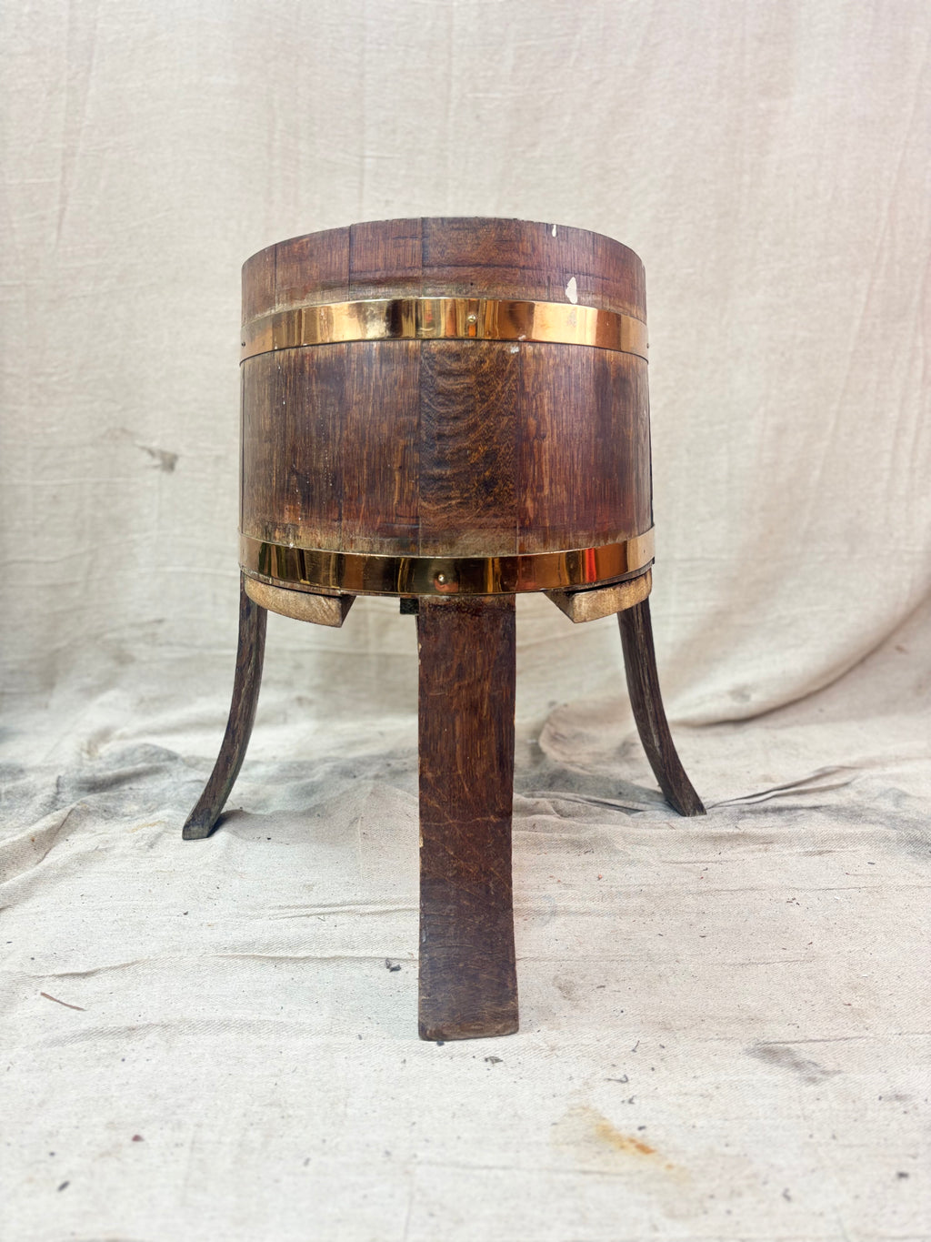 Wooden barrel-shaped table with brass banding on a textured white background
