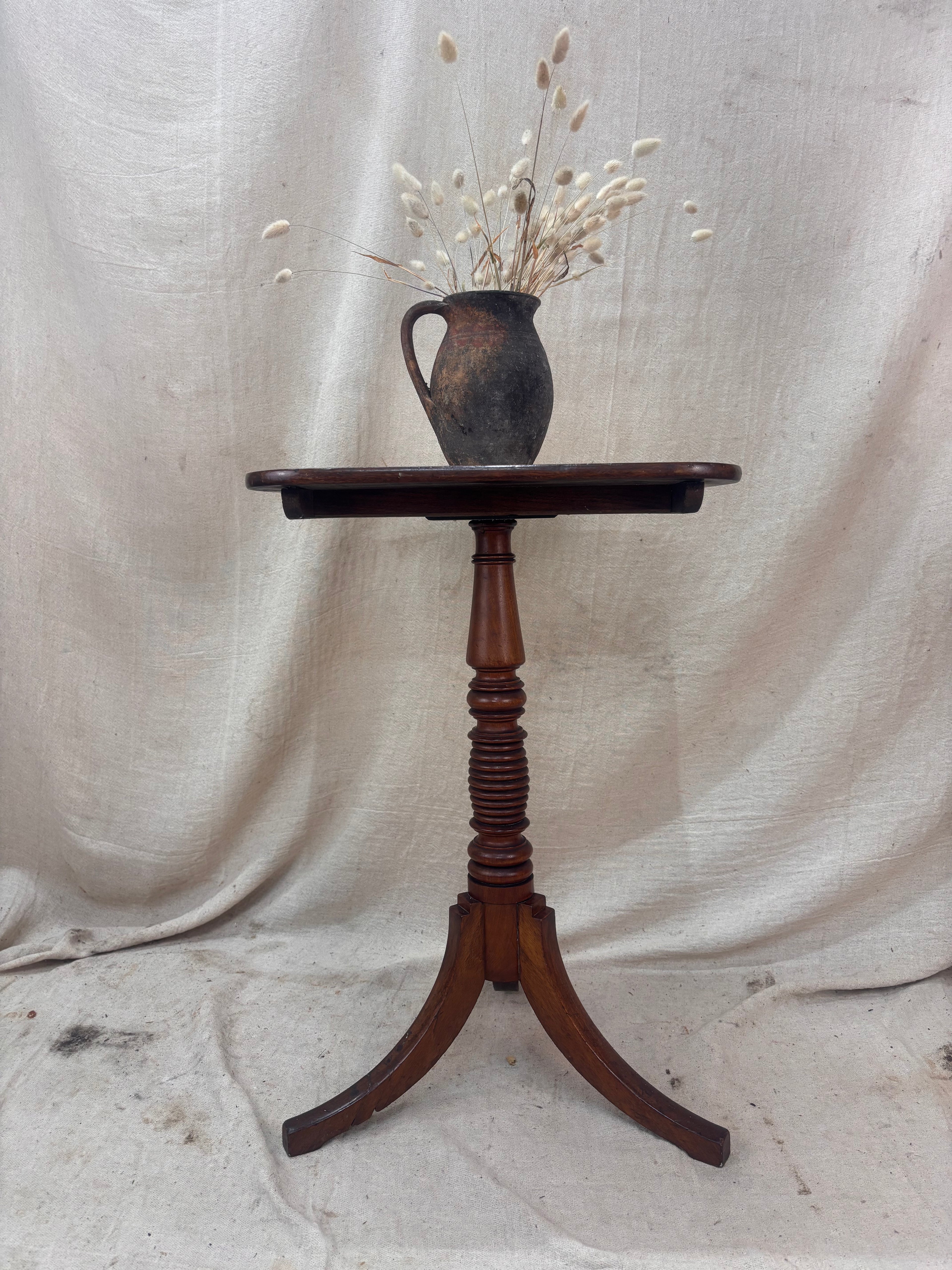 Wooden pedestal table with a vase of dried flowers on a textured white background
