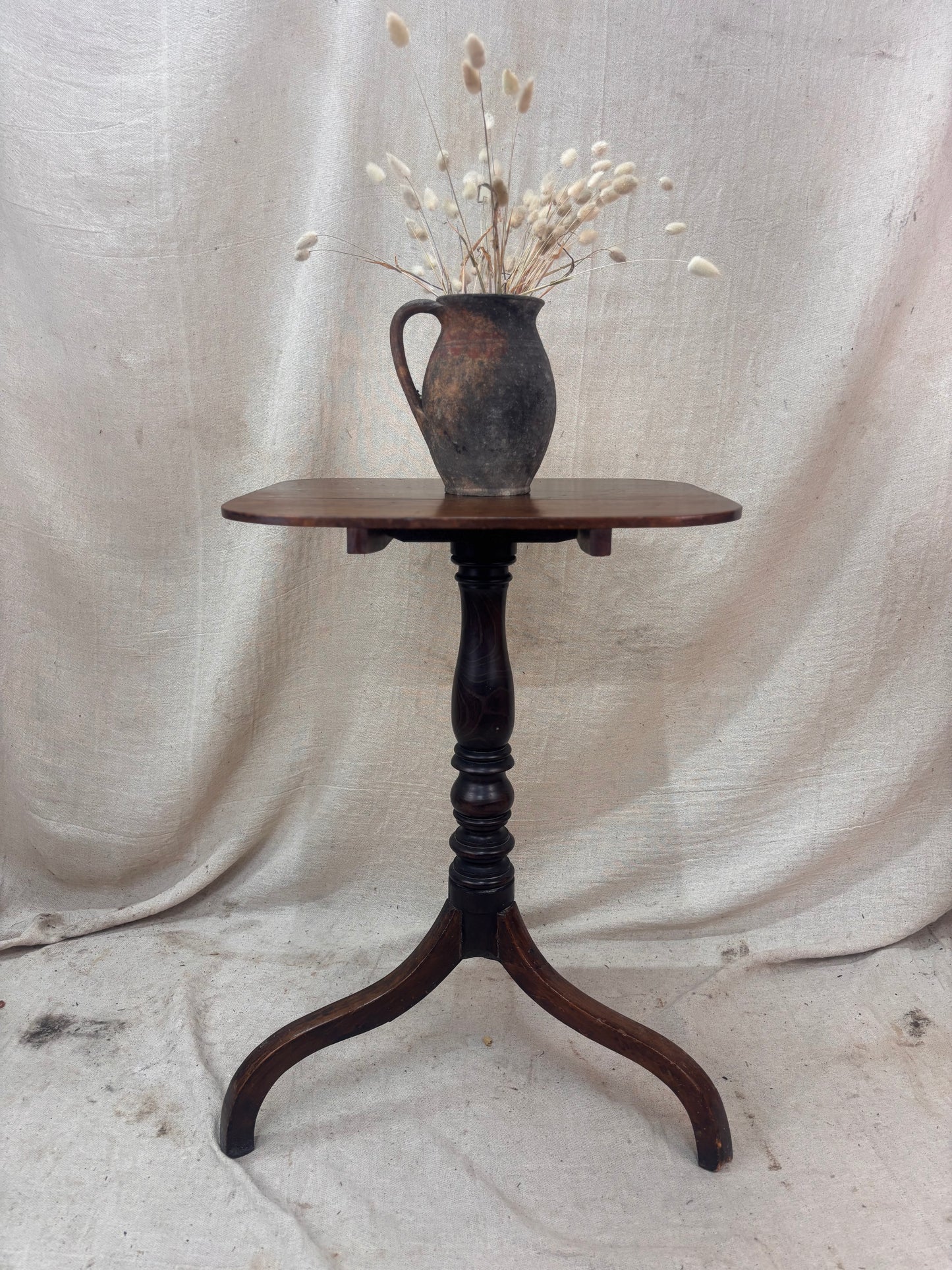 Wooden table with a vase of dried flowers on a draped fabric background
