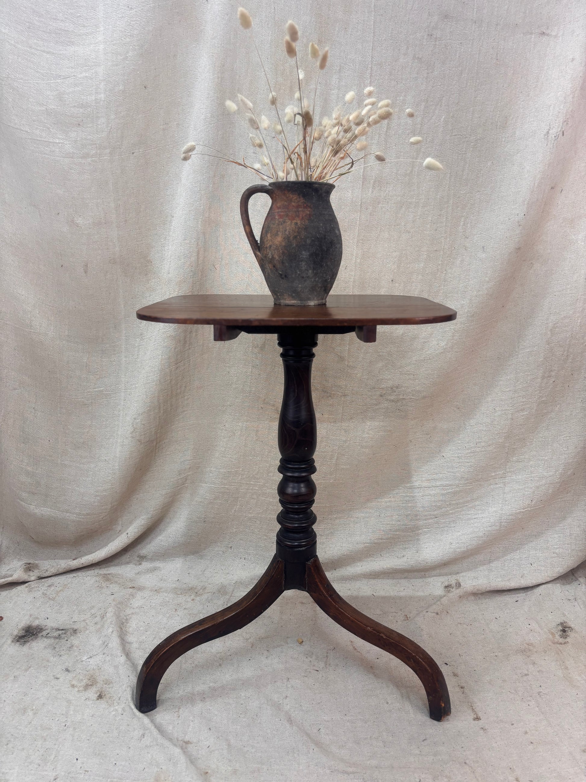 Wooden table with a vase of dried flowers on a draped fabric background