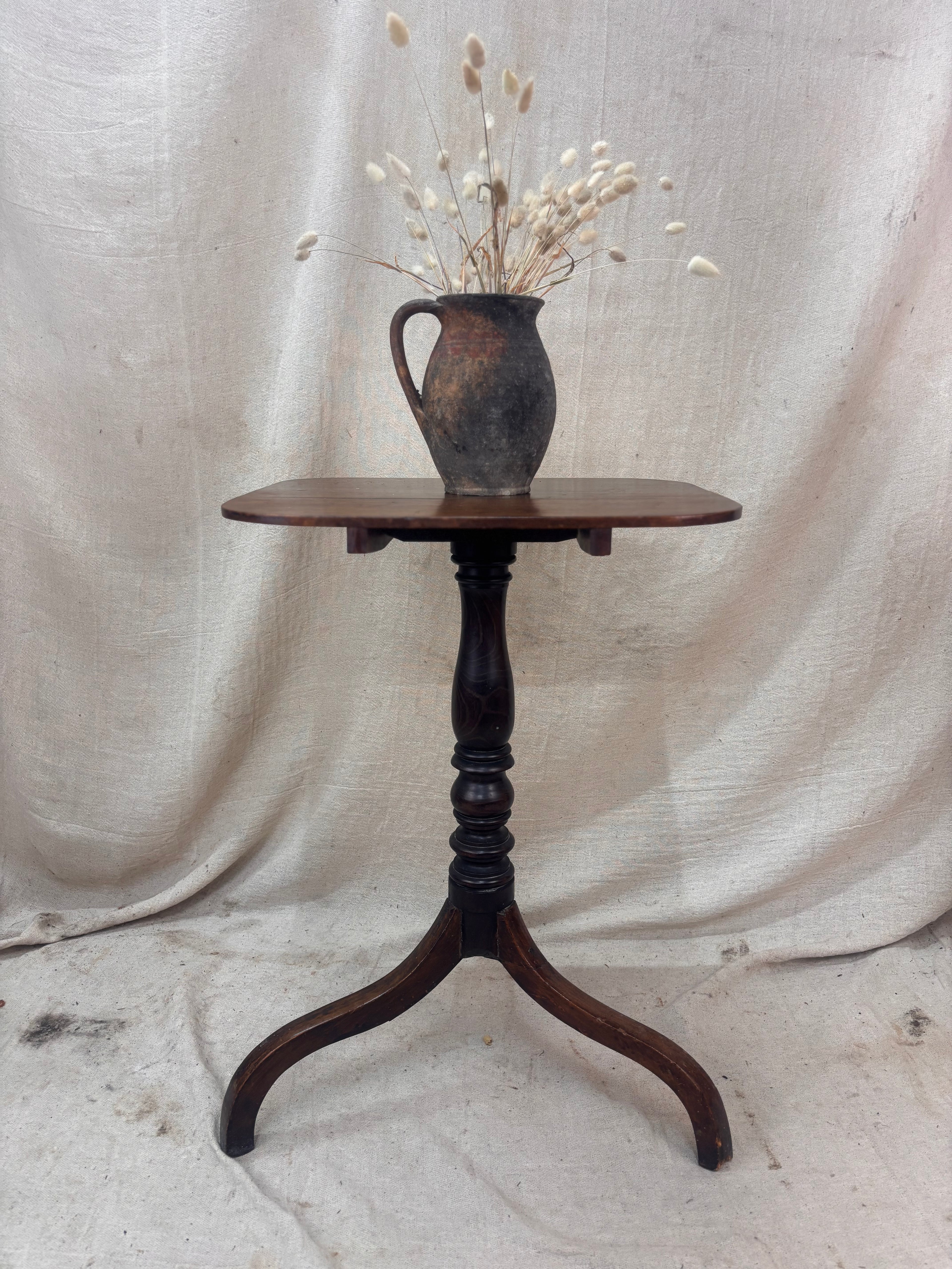 Wooden table with a vase of dried flowers on a draped fabric background