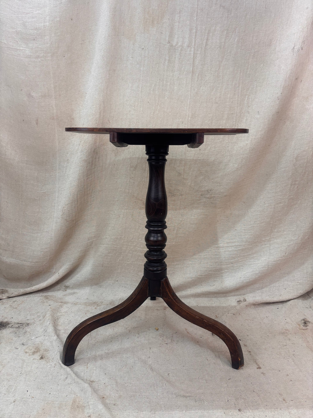 Wooden pedestal table against a beige fabric background