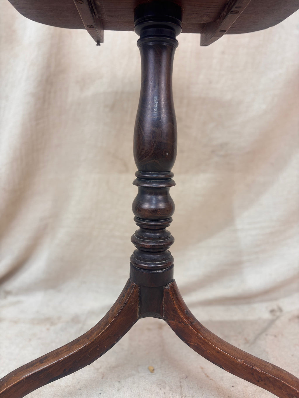 Close-up of a wooden pedestal table base on a beige fabric background