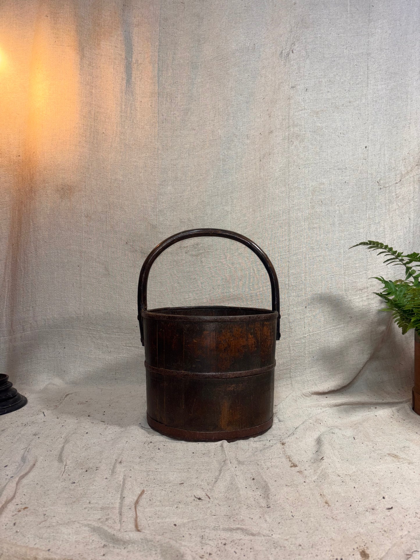 Rustic wooden bucket on a textured white surface with a plant in the corner